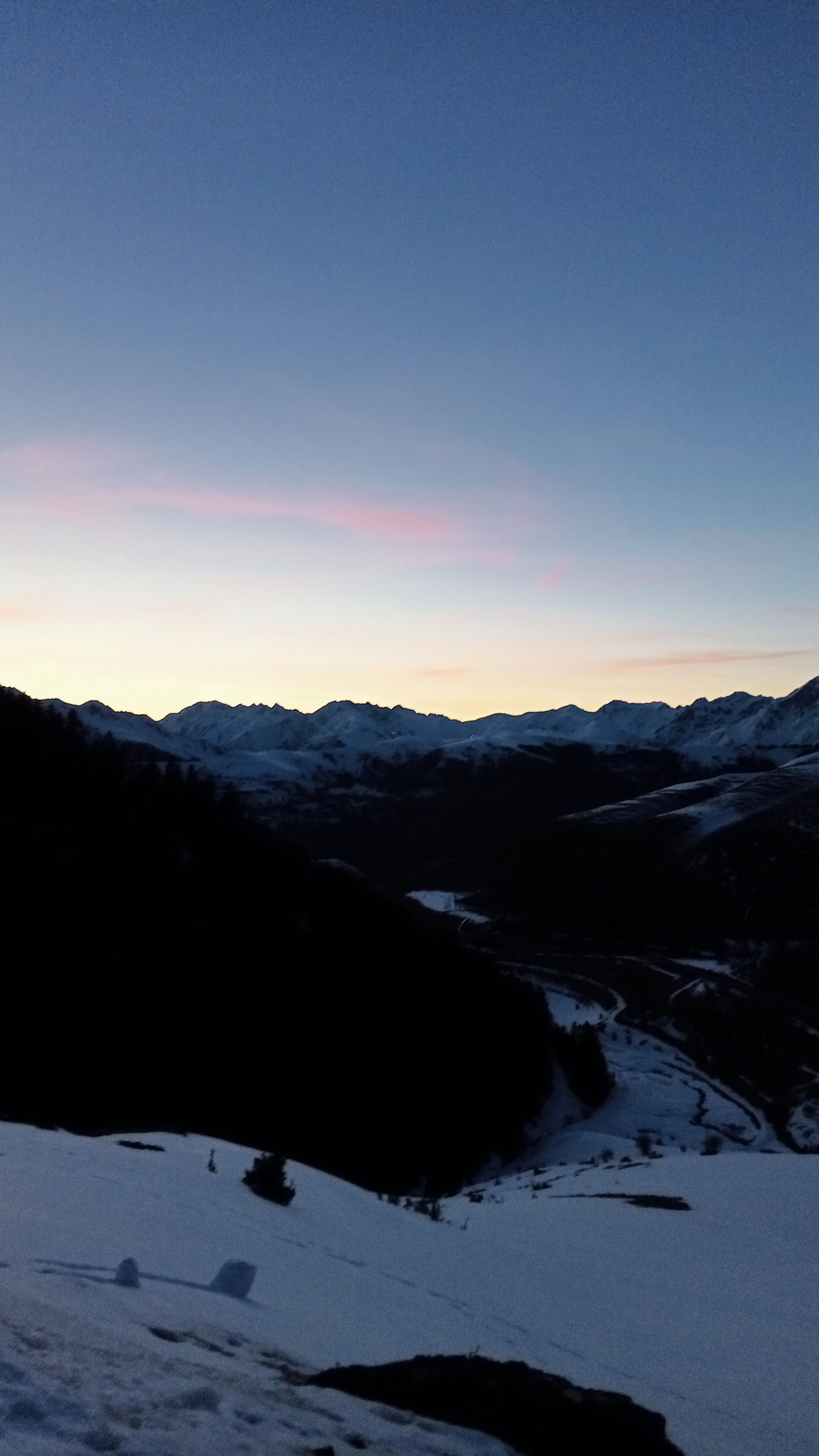 Paysage de montagnes enneigées au coucher du soleil avec un ciel clair et quelques nuages roses.