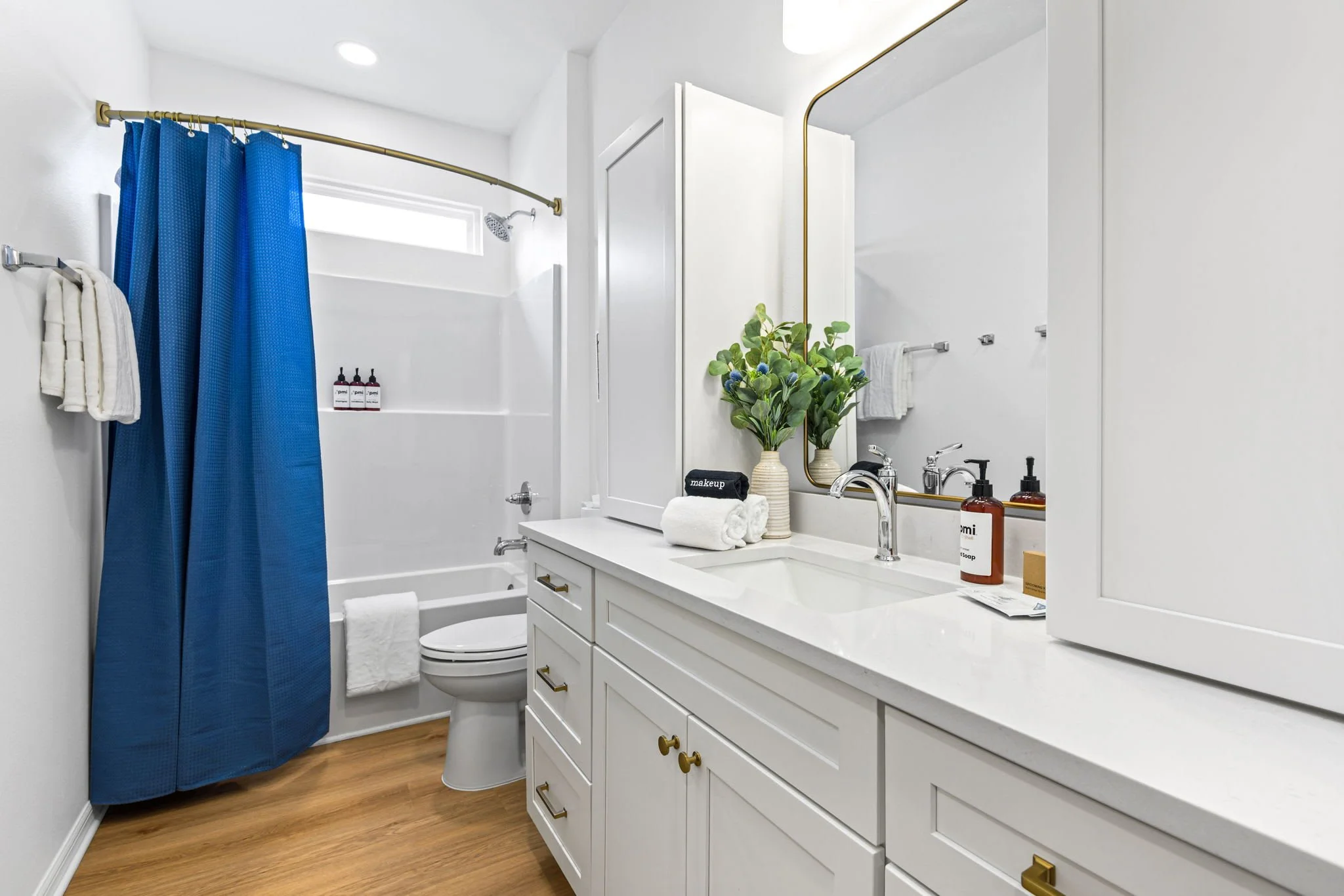 A bright bathroom with a white vanity, a mirror, and a shower with a blue curtain.
