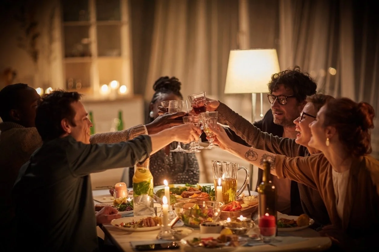 Group of people gathered around a dinner table at night, raising their glasses in a toast, with lit candles and food on the table.