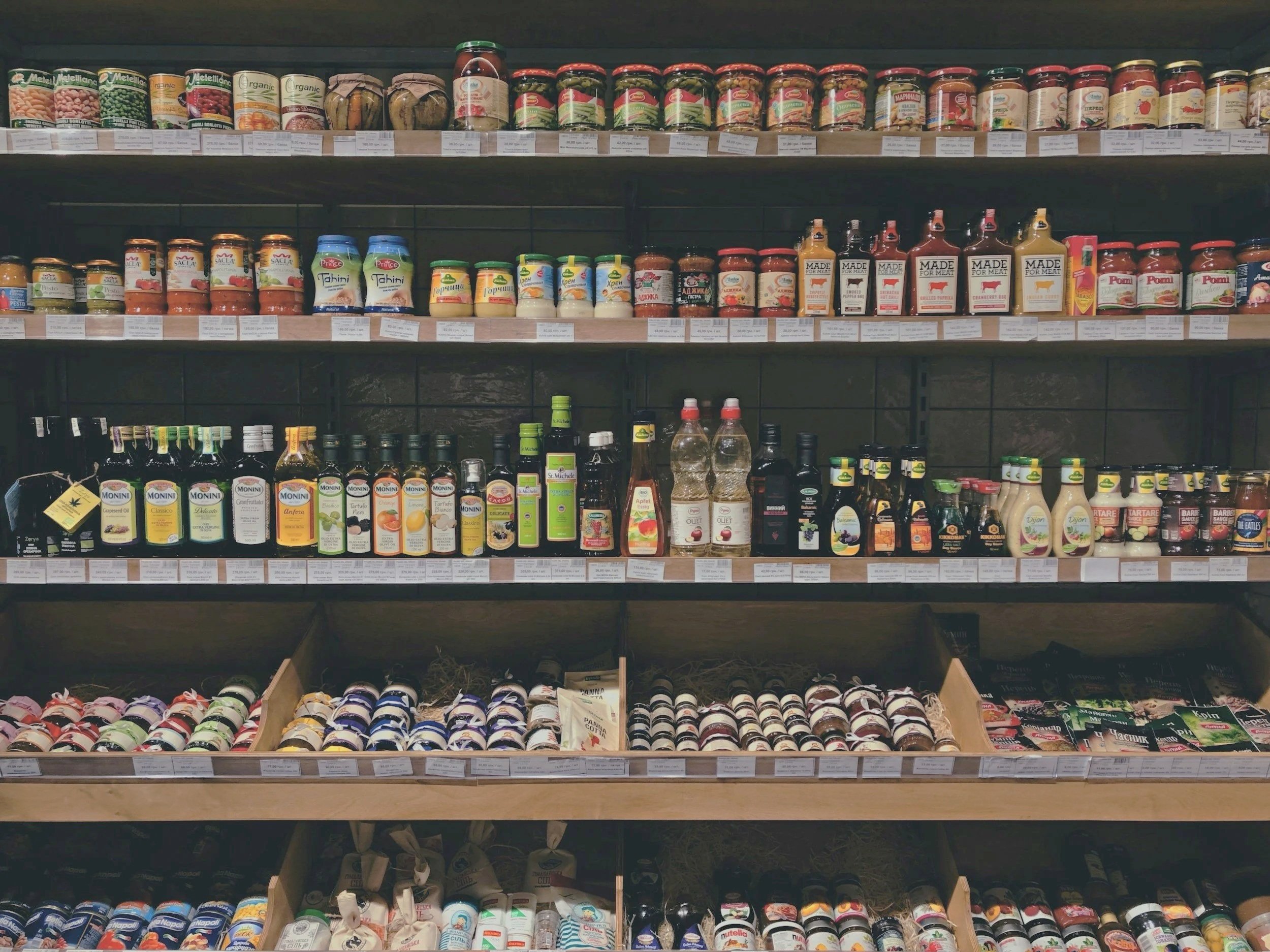 Shelf in a grocery store with various canned and bottled food products, including beans, sauces, and condiments.