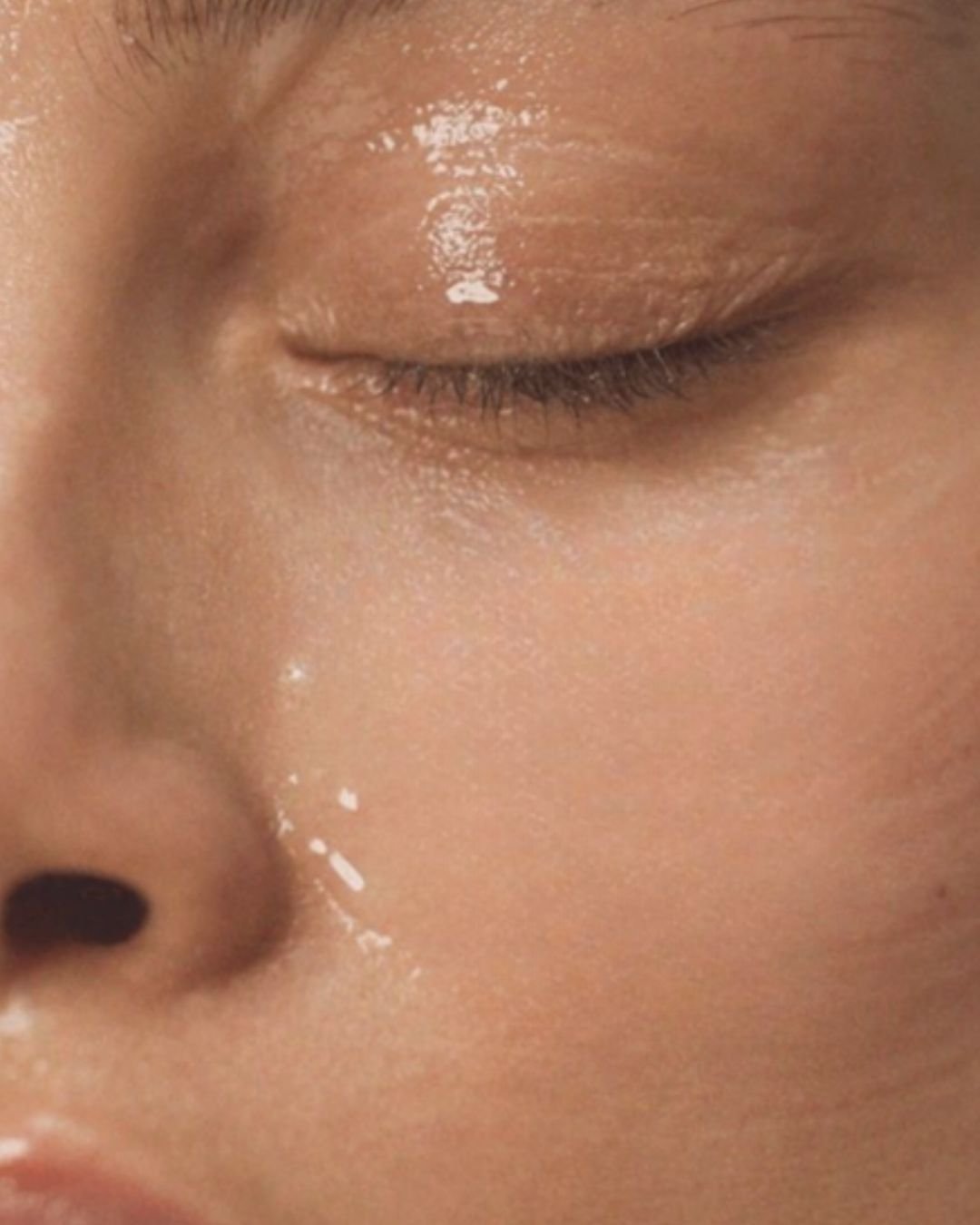 Close-up of a person's face with closed eye, focusing on the skin, eyelid, and nose, with a shiny appearance on the skin around the eye.
