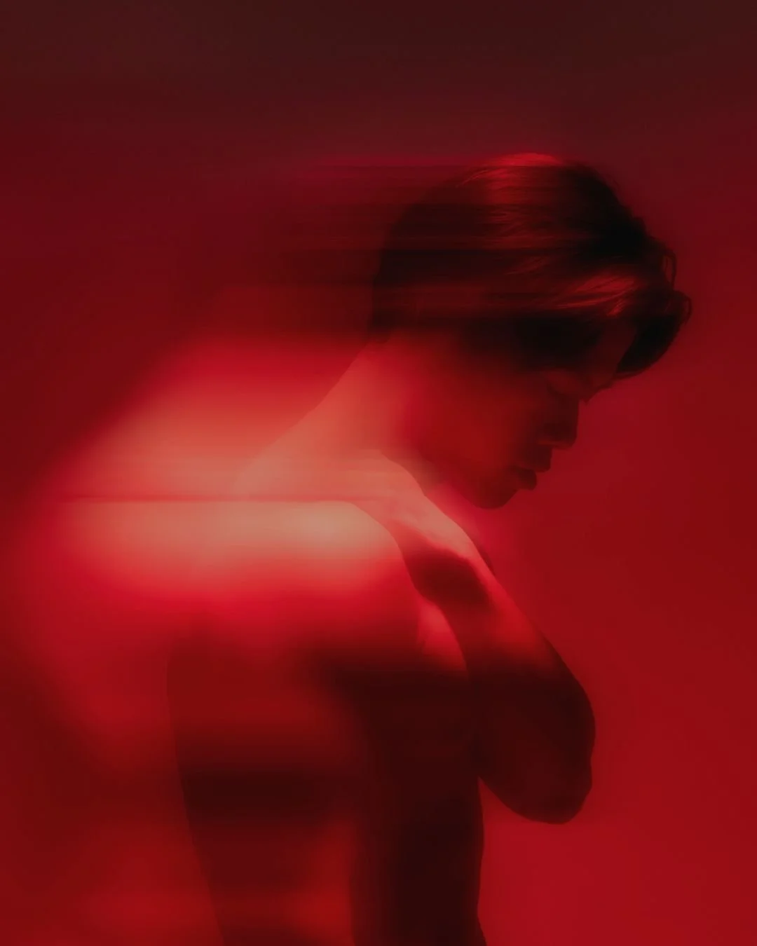 A person with short hair, looking down, surrounded by a red-colored glow, with a blurry motion effect.