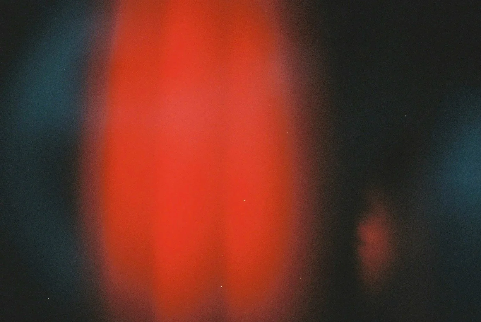 An out-of-focus abstract image with a blurred red streak in the center, surrounded by dark and blueish areas with faint stars visible in the background.