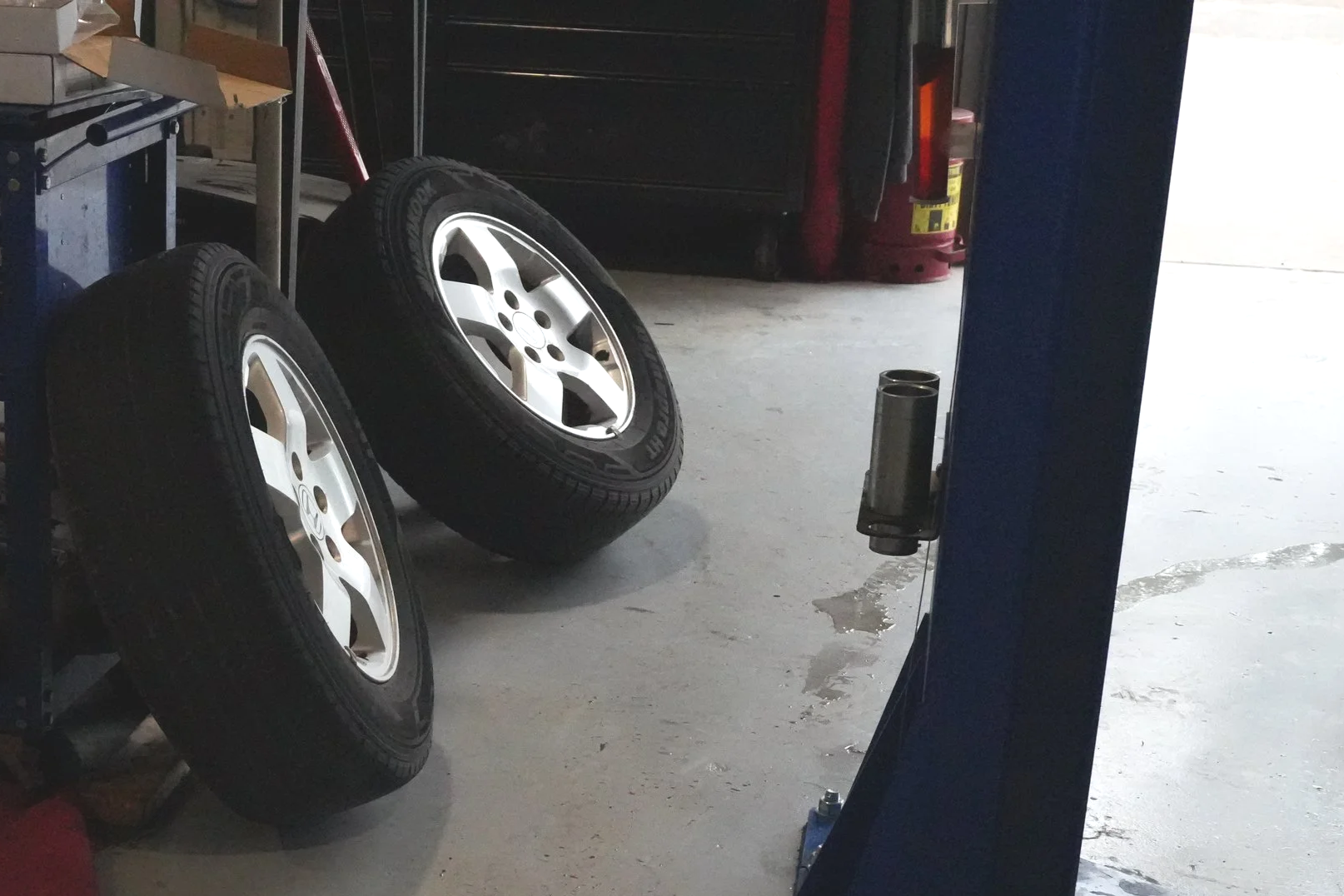 Two tires with silver hubcaps leaning against a tool cart in a garage or workshop.