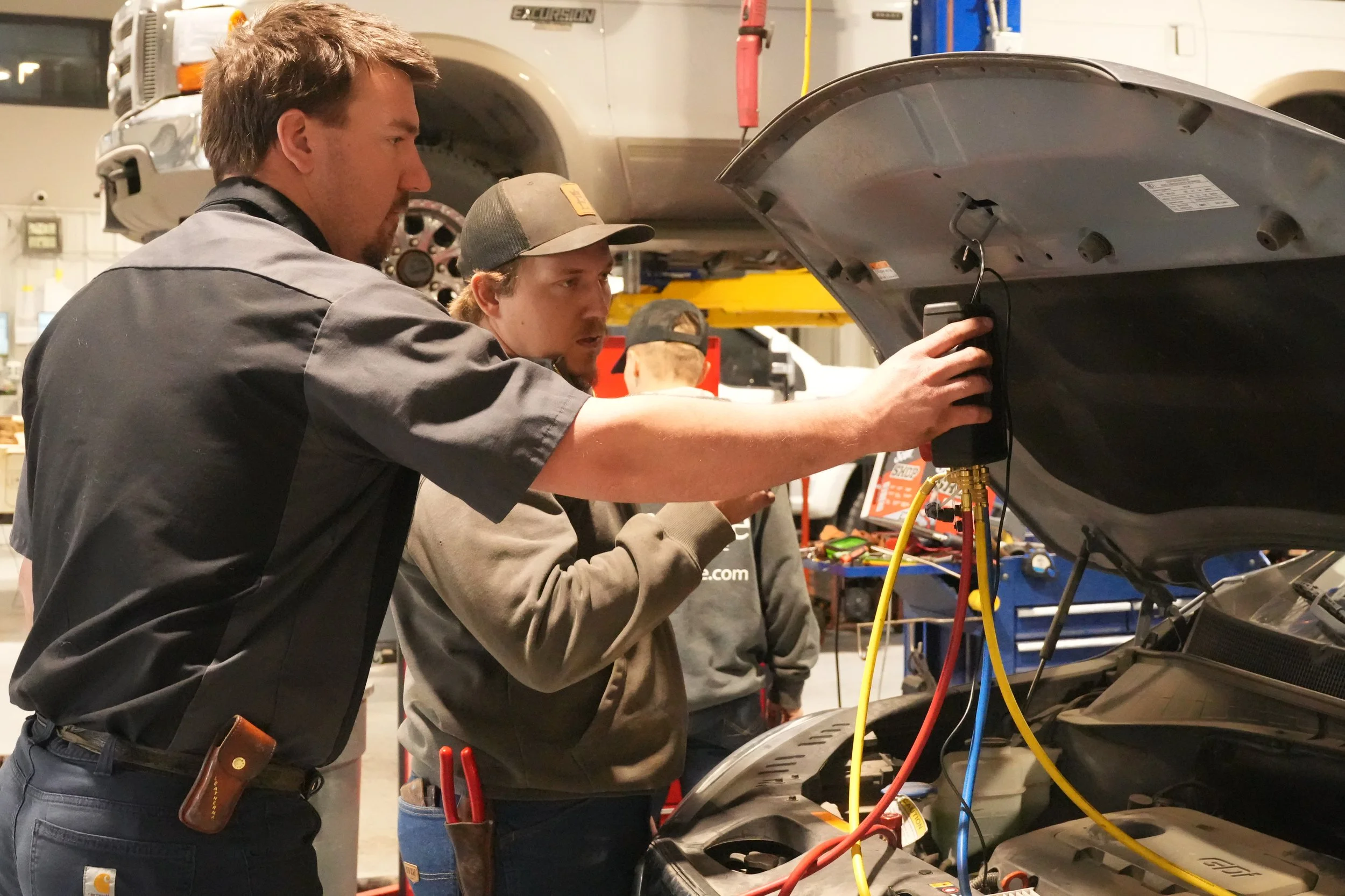 Three men working on a car engine in an auto repair shop.