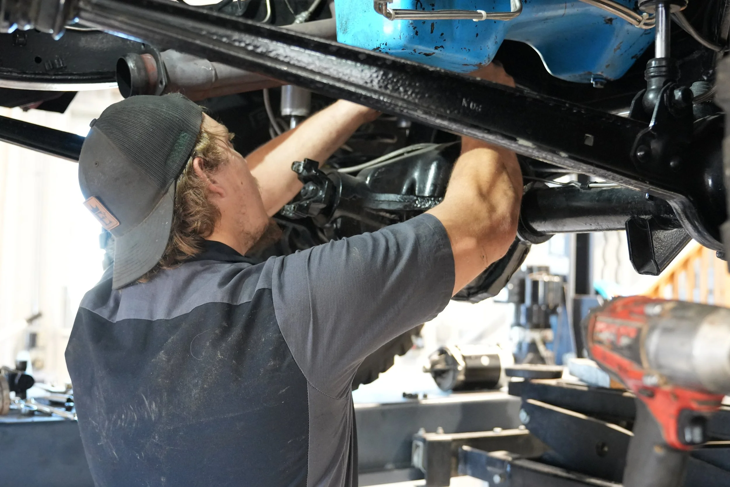 Auto repair technician servicing suspension and drivetrain underneath a vehicle at Empire Repair
