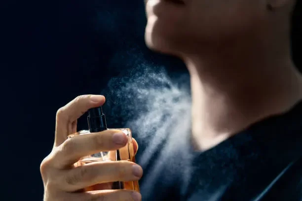Person spraying perfume from a bottle onto their neck.
