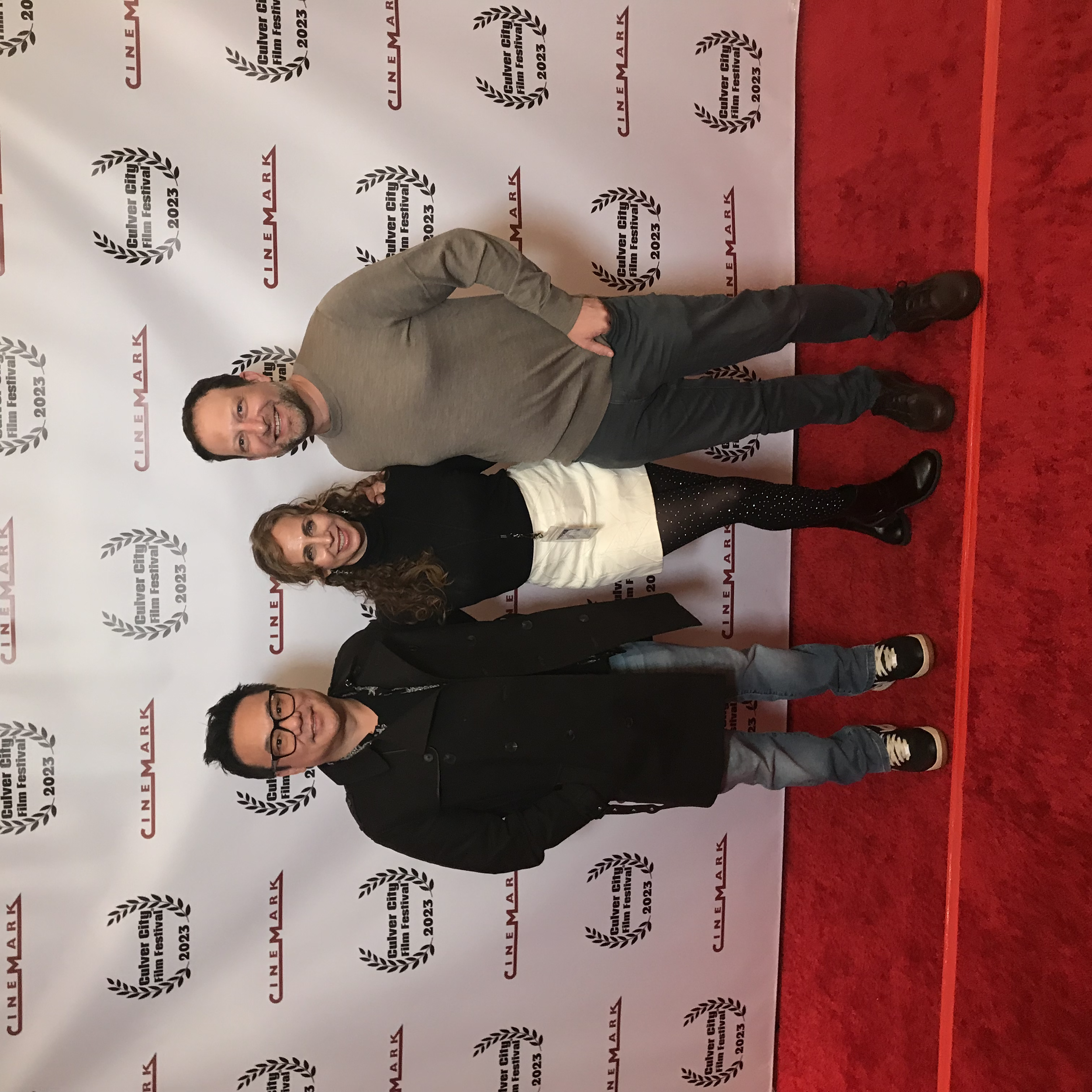 Jimmy Shin, Jennifer Lieberman and Matt Saigon on red carpet in front of a white backdrop with black laurel wreaths and red text, at the Culver City Film Festival 2023 with their award-winning short film "The Penis Fairy"