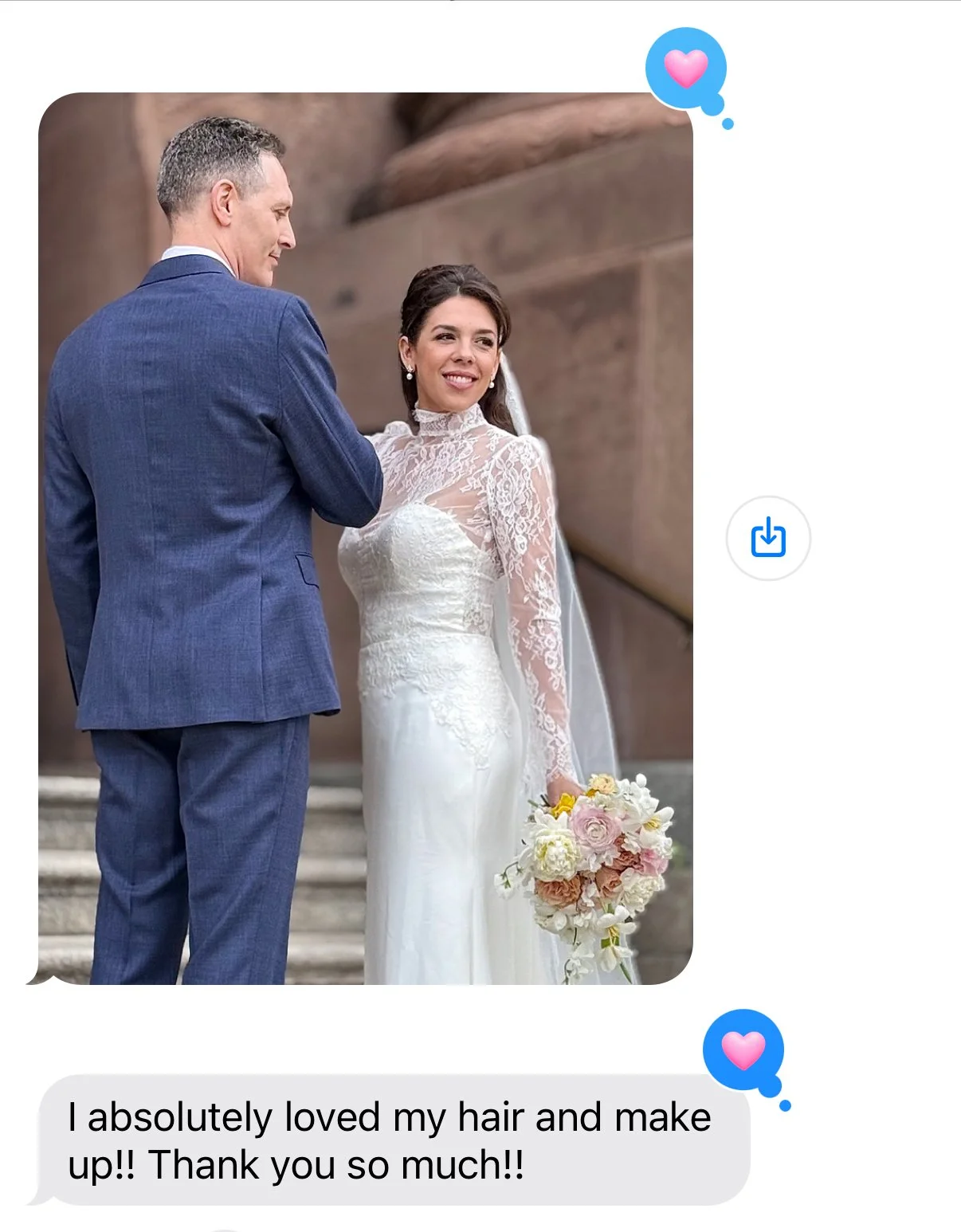 A bride in a white lace wedding dress holding a bouquet of flowers, standing next to a groom in a blue suit, outdoors with stone steps and large rocks in the background.