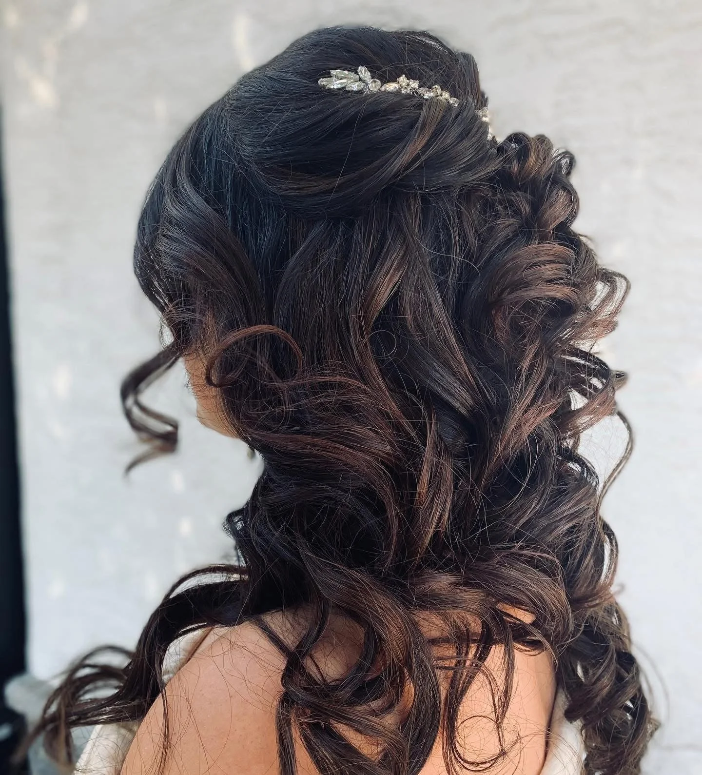 A woman's head with beautifully styled dark brown, curly hair adorned with a decorative silver hairpiece.