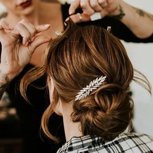 A stylist is creating an elegant updo hairstyle with a decorative hair accessory in a woman's hair.