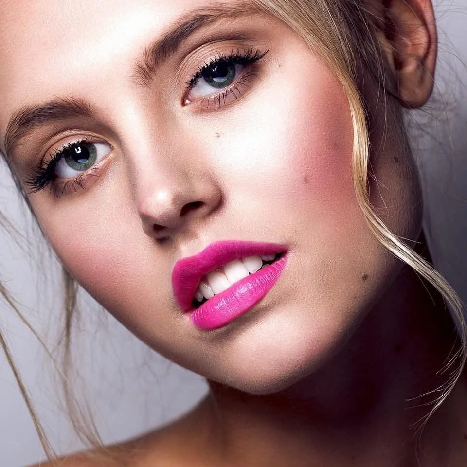Close-up portrait of a young woman with blonde hair, blue eyes, pink lipstick, and light makeup.