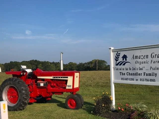 Red tractor on a grassy field with a white sign for Amazon Grow Organic Farm in front of it.