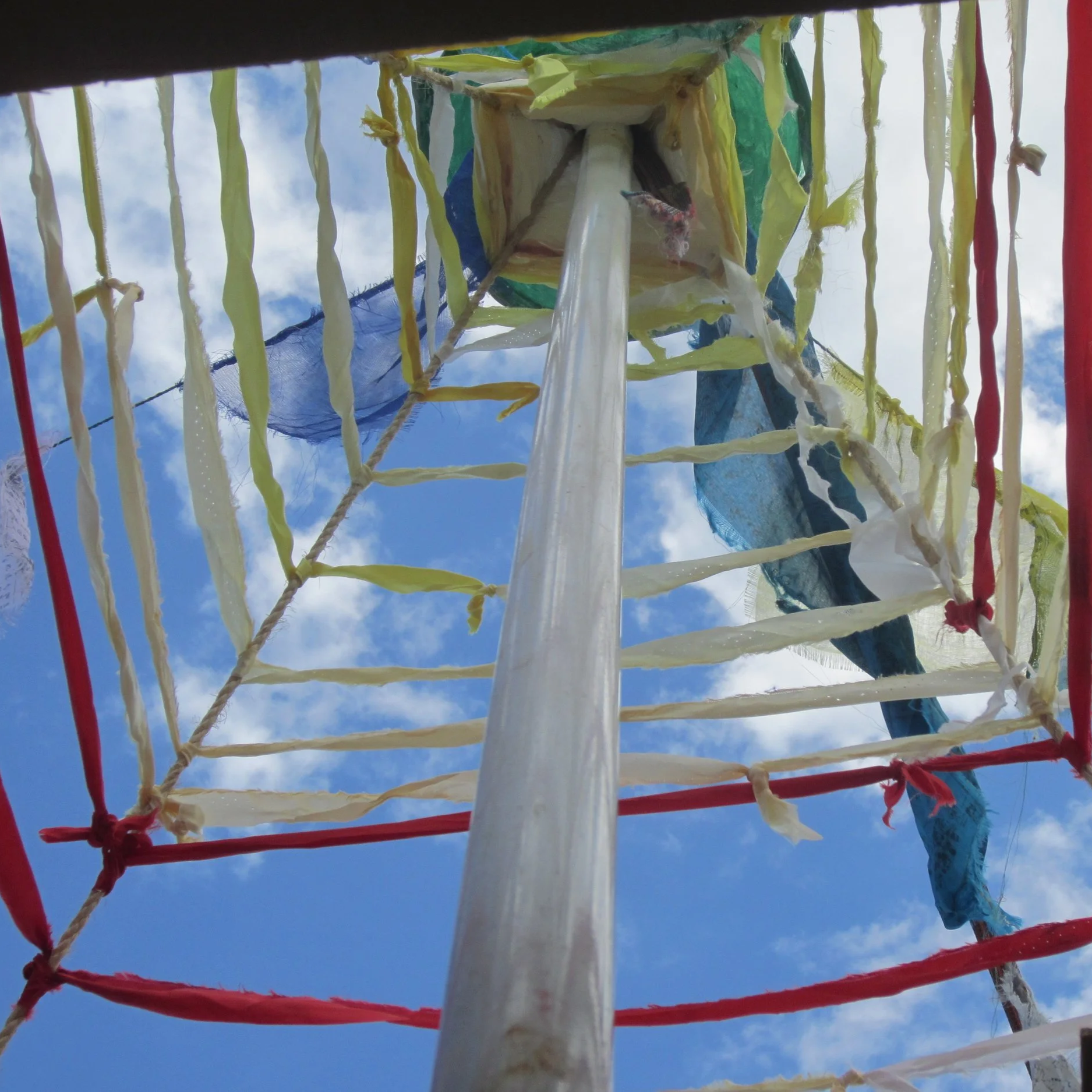 Looking up at colorful prayer flags and strings of yarn against a blue sky with clouds.