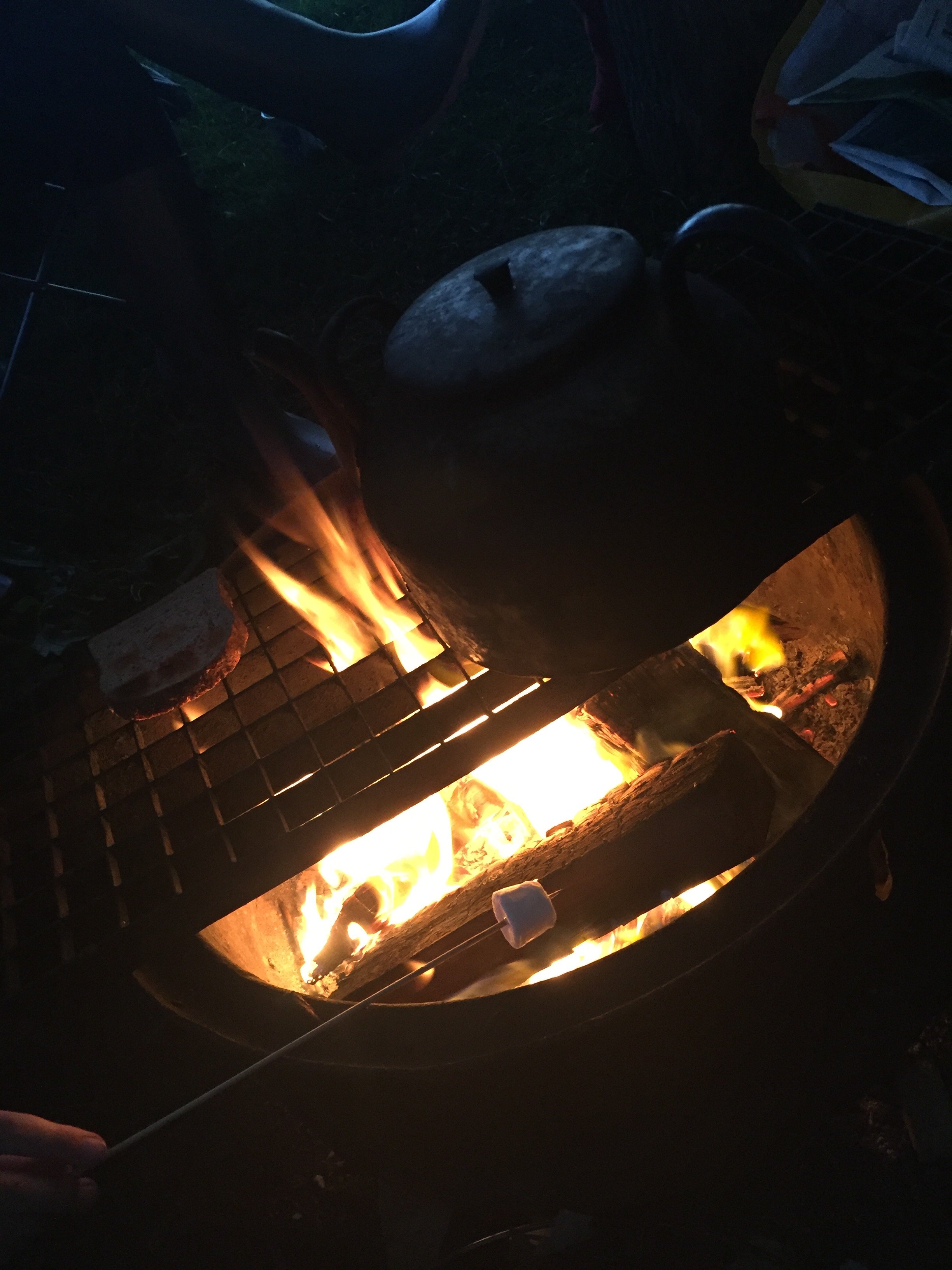 Fire burning inside a fire pit with a metal lid and bricks around it.