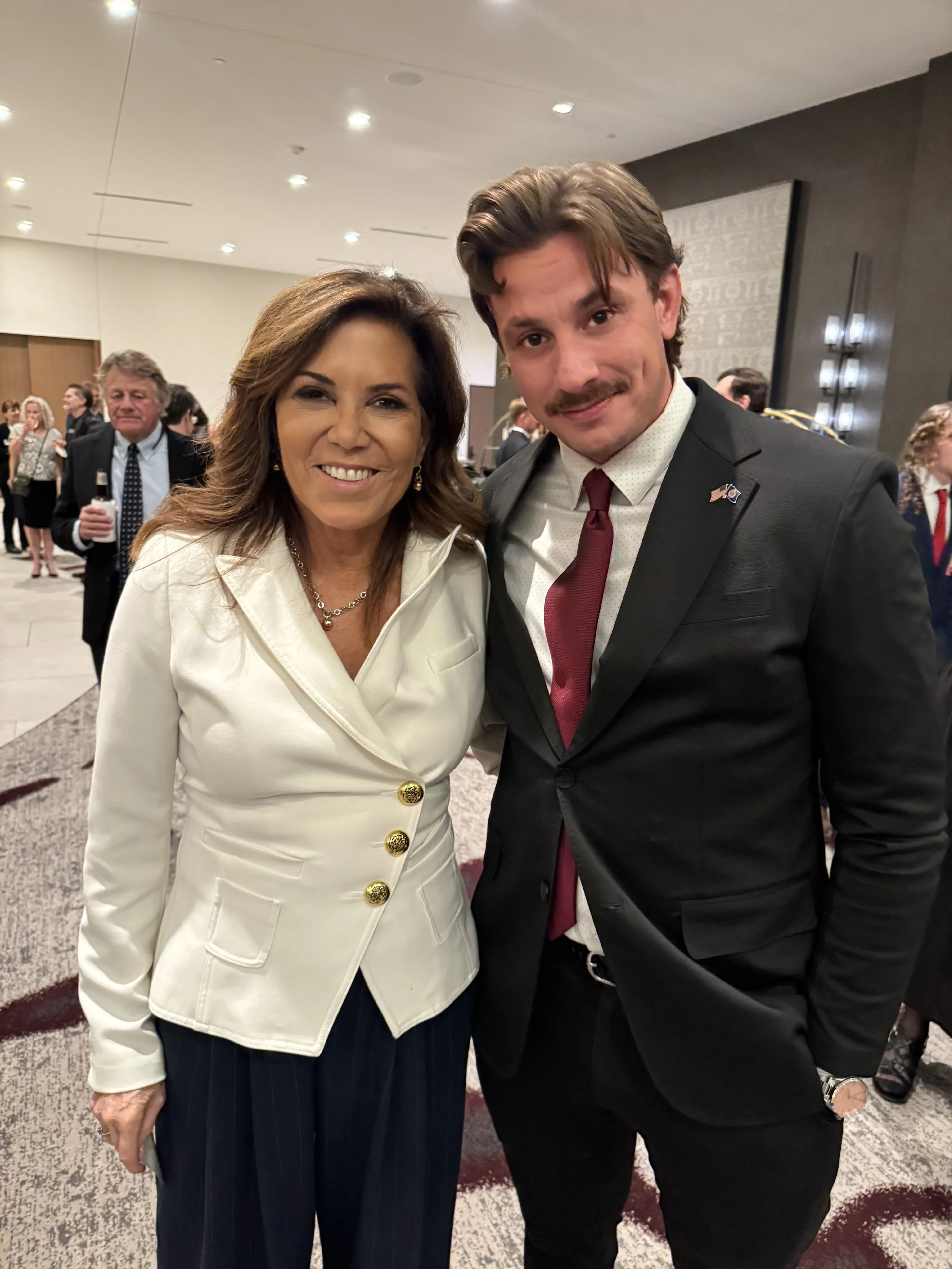 AJ Gubash standing with Michele Tafoya at an indoor event, both smiling for a photograph.