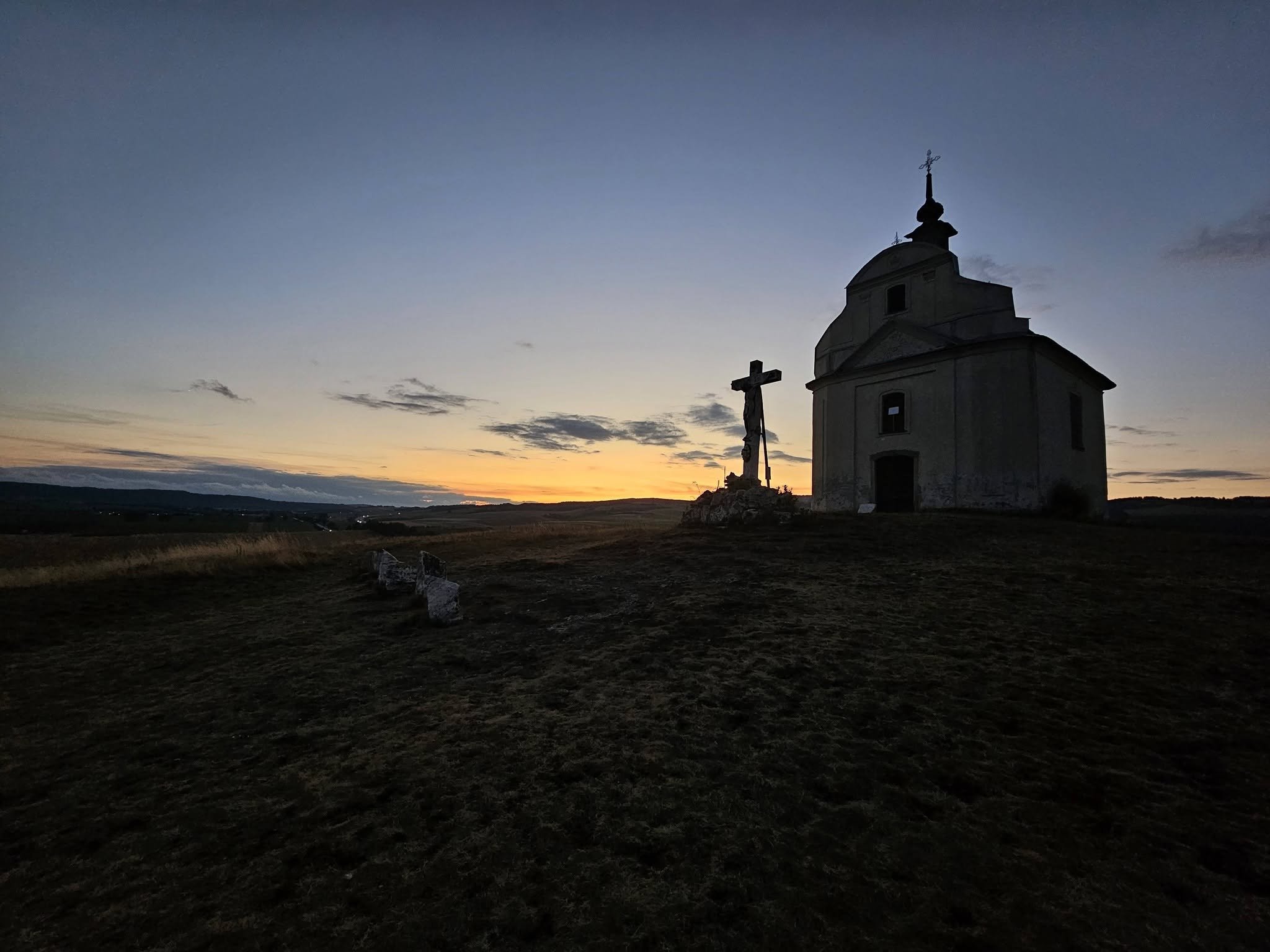 Historic chapel and roadside cross silhouetted against a colorful sunset sky during an August 2026 visit to Slovakia.