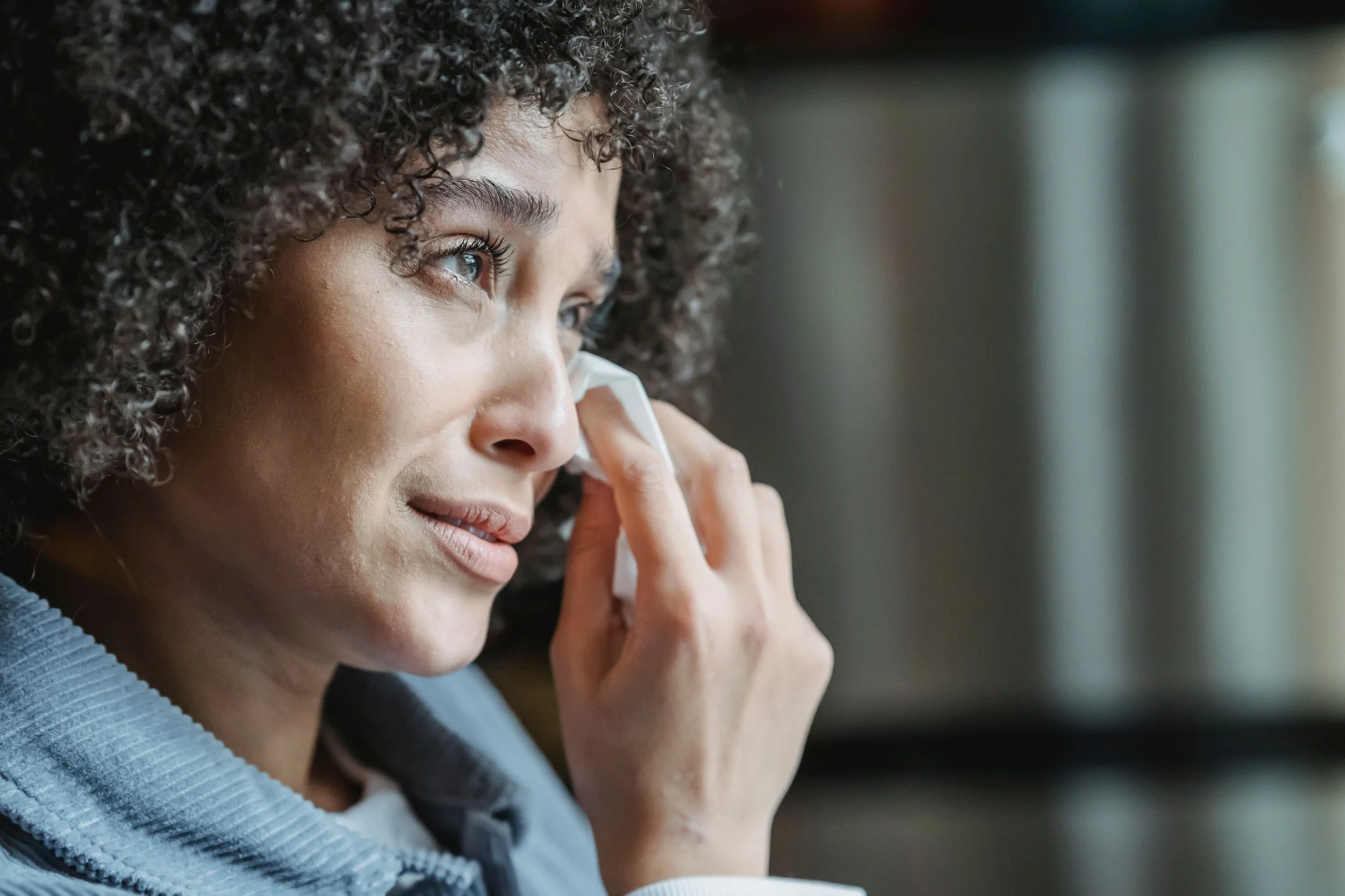 Close-up of a curly-haired woman wiping her eye with a tissue