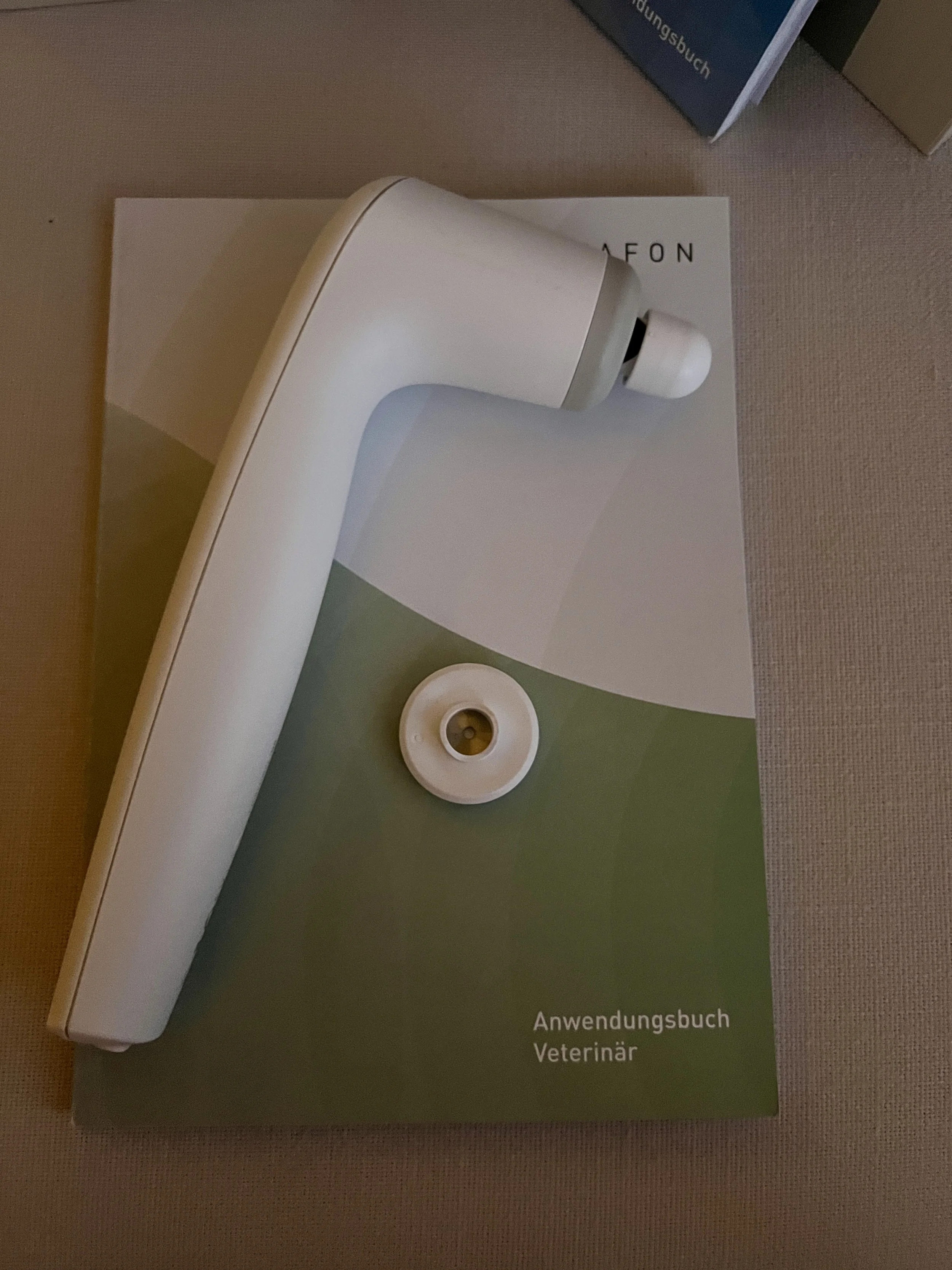 Ein weißer medizinischer Apparat liegt auf einem grünen Buch mit schwarzen Text. Das Buch hat die Titel 'Anwendungsbuch Veterinär'.