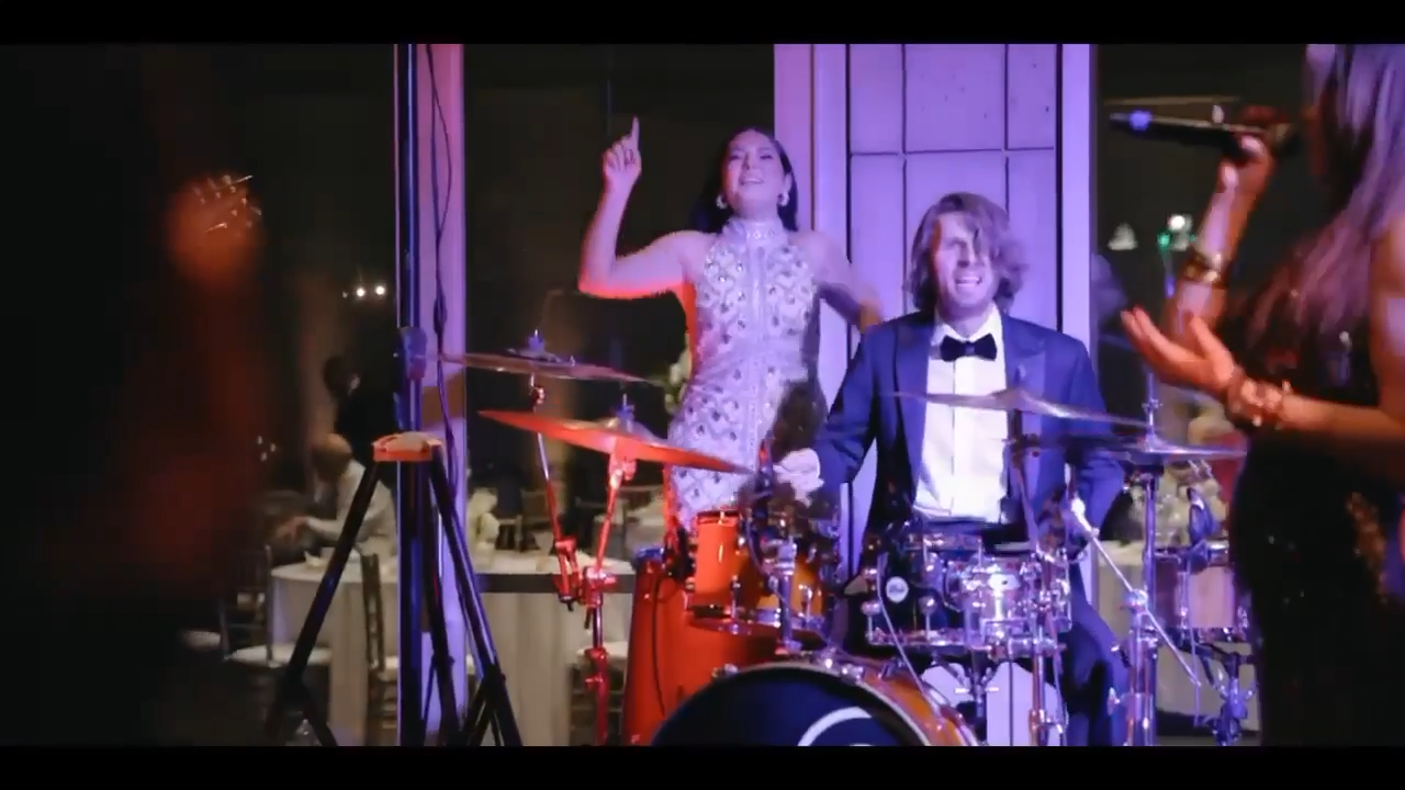 People enjoying a live band performance at a social event or party, with a woman singing into a microphone and a woman dancing behind the drummer.