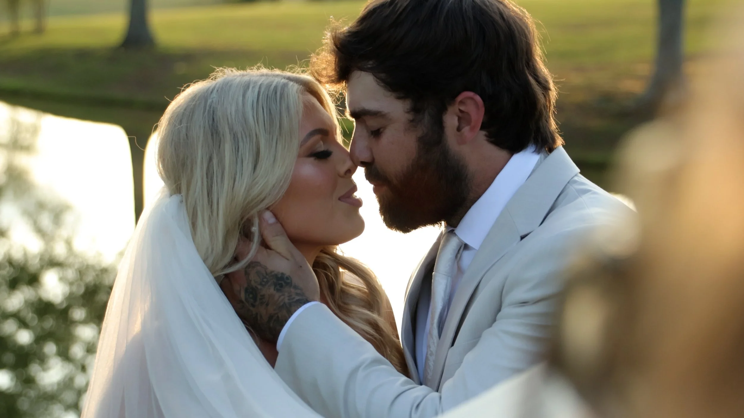 A bride and groom share a close moment outdoors, with their foreheads touching and eyes closed, during their wedding ceremony in a natural setting with trees in the background.