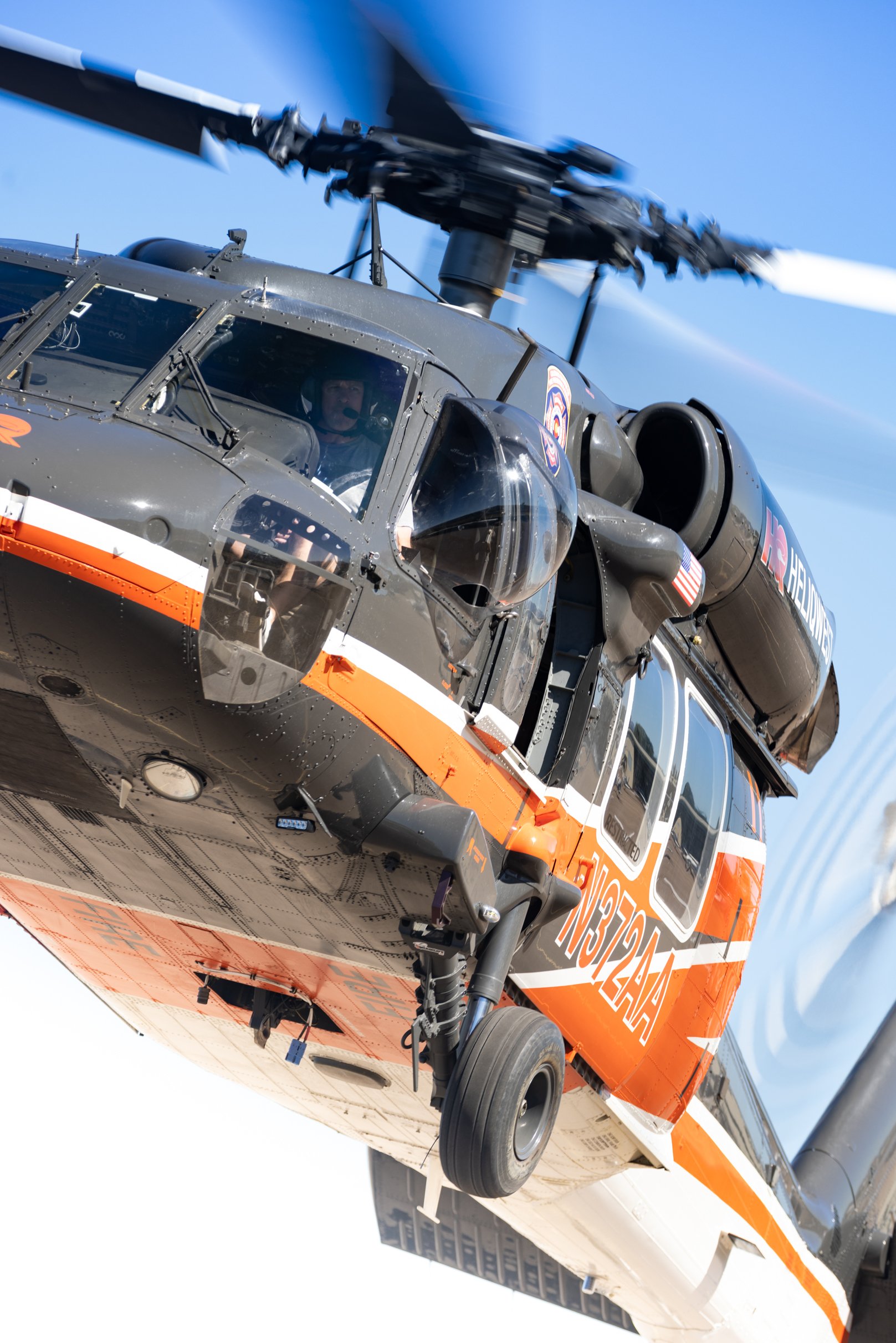 Close-up of an orange and black helicopter with the number 43 and US flag on the side, flying against a blue sky.