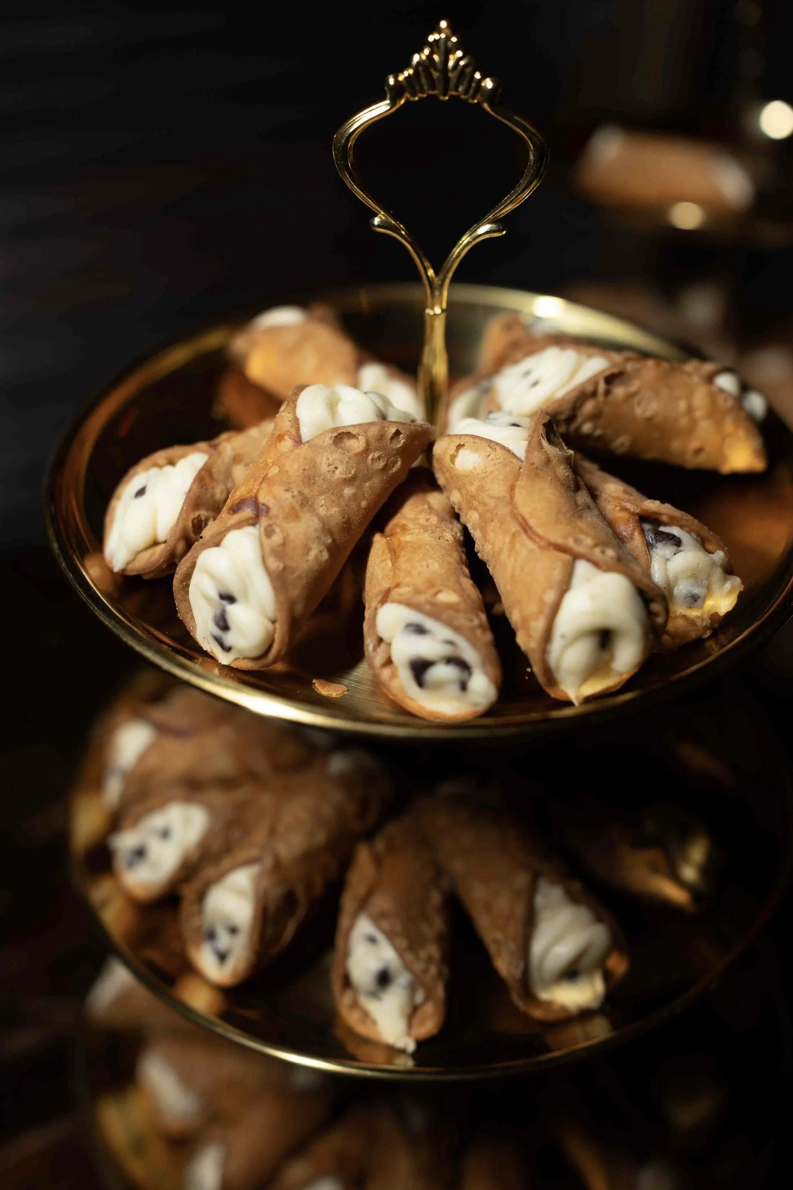 Golden bowl filled with cannoli, a dessert with a crispy shell and creamy filling, on a dark background.