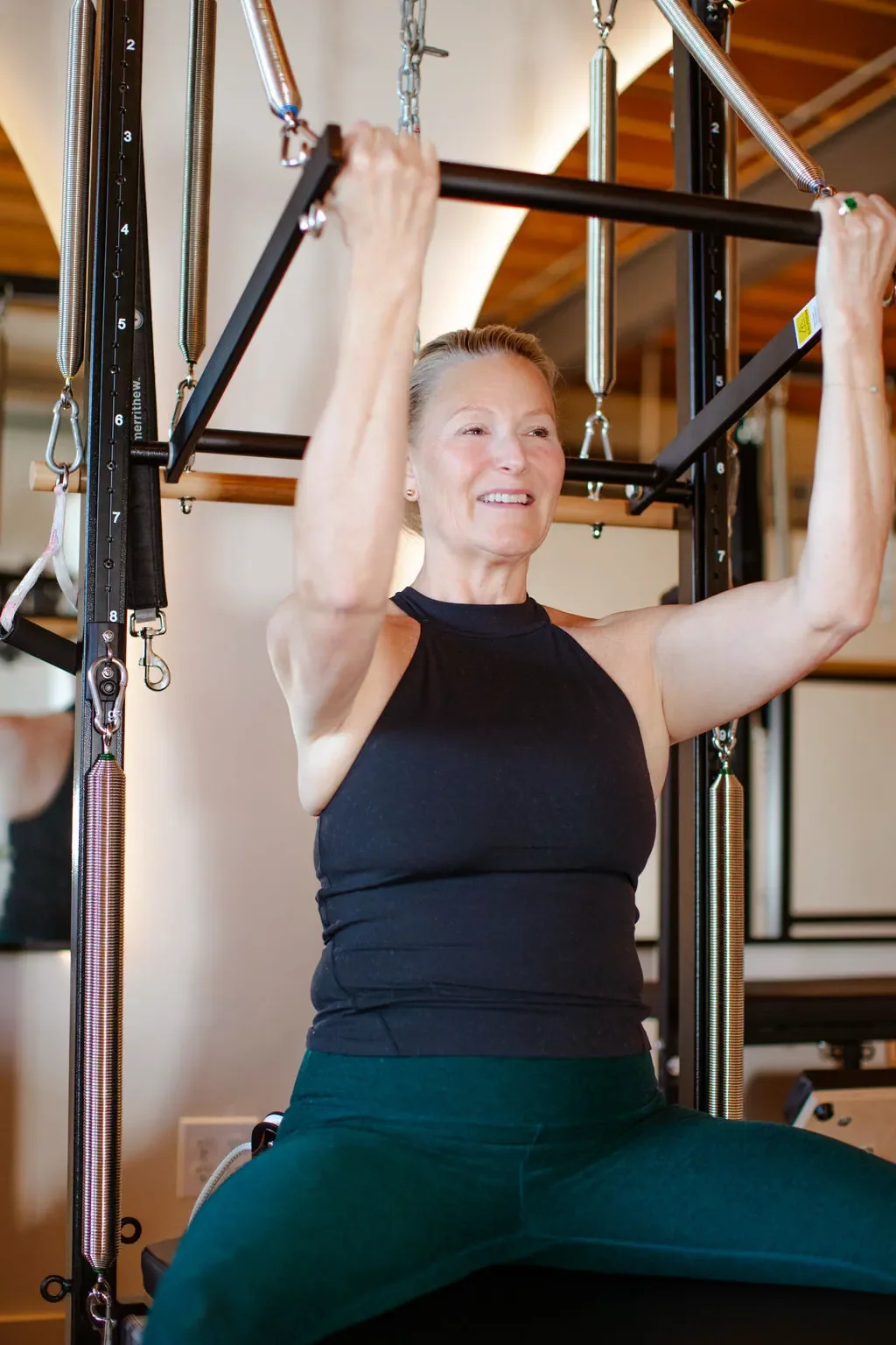 A woman exercising on a Pilates reformer machine in a fitness studio.