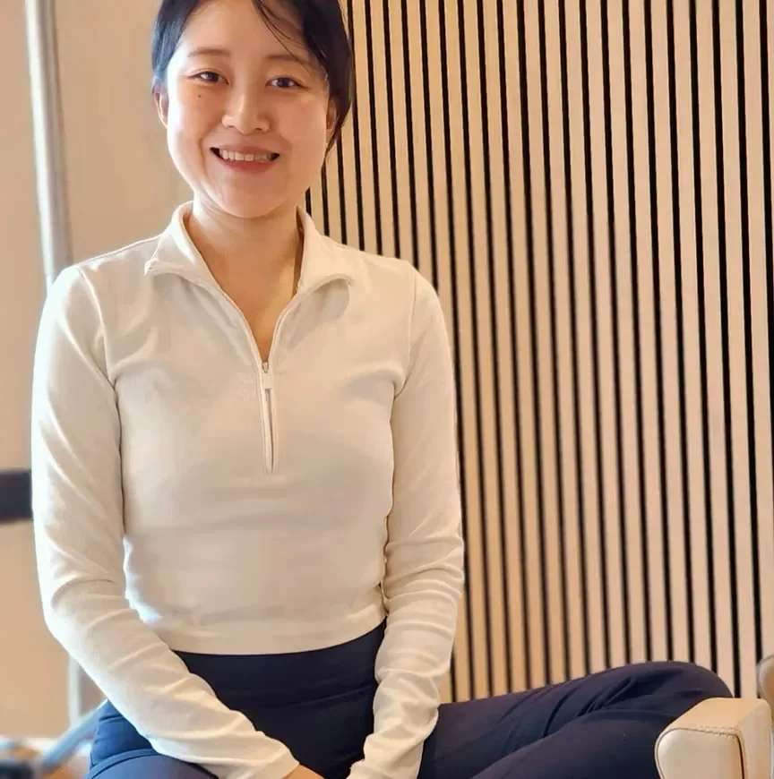 A woman sitting in front of a wooden slatted wall, smiling at the camera.