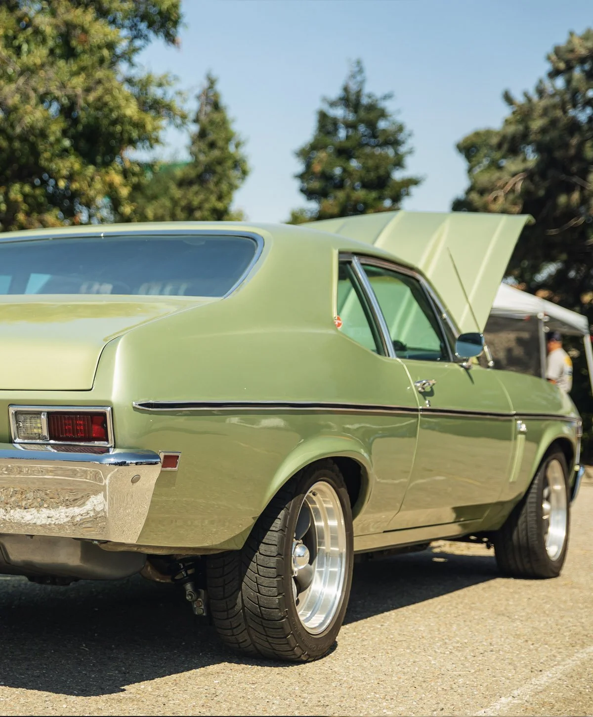 A vintage green car with a hatchback, parked outdoors on a sunny day, with trees in the background.