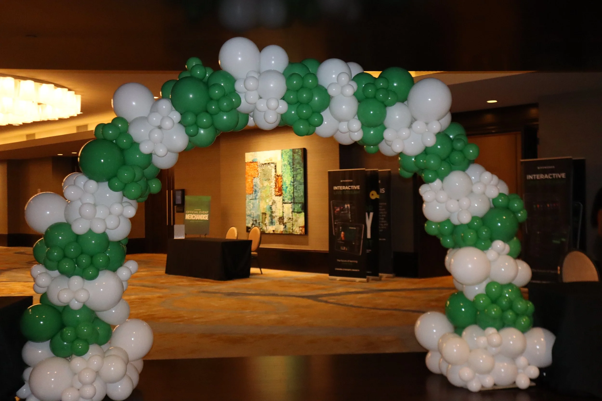A decorative arch made of white and green balloons set up in an indoor venue.