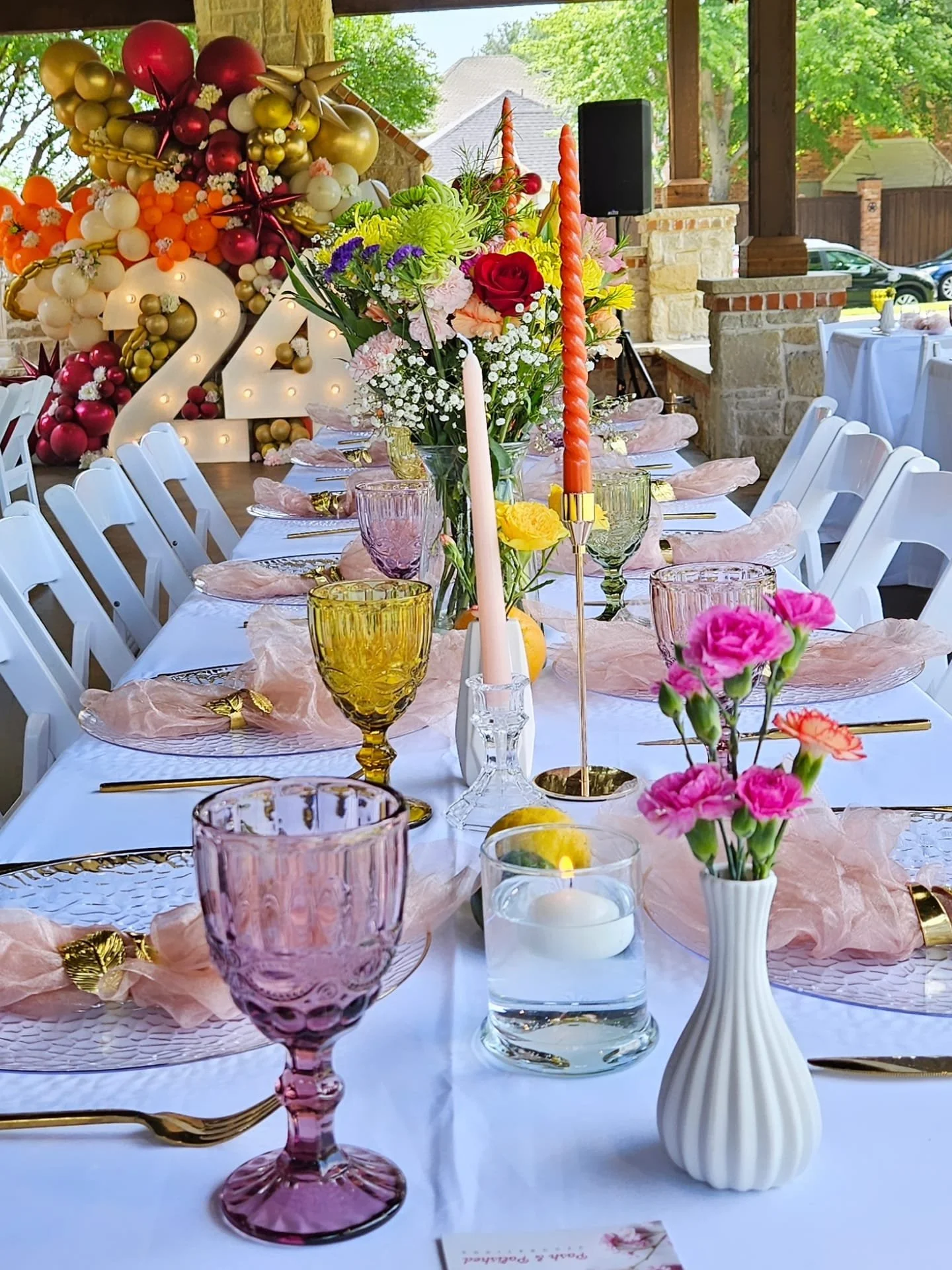 Decorated banquet table with pink and gold accents, floral centerpieces, colorful candles, and balloons forming the number 22 in the background, set for a celebration or party.