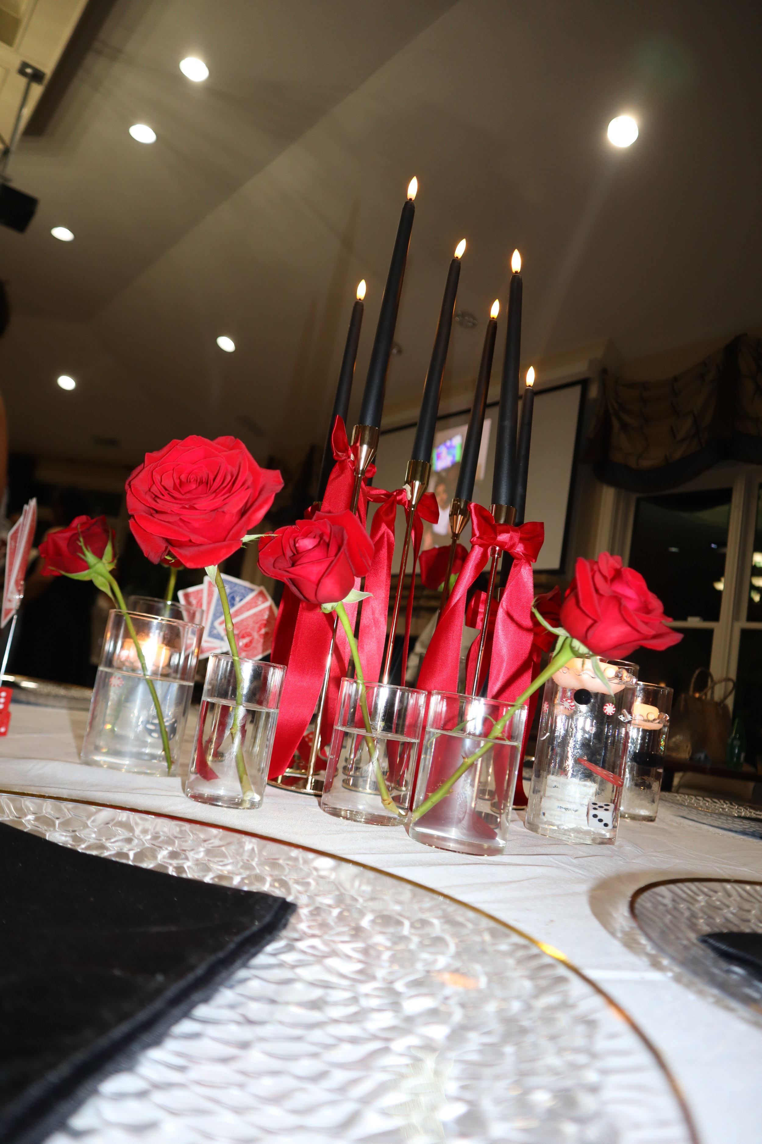 Red roses and black candles decorated with red ribbons on a table at an indoor event.