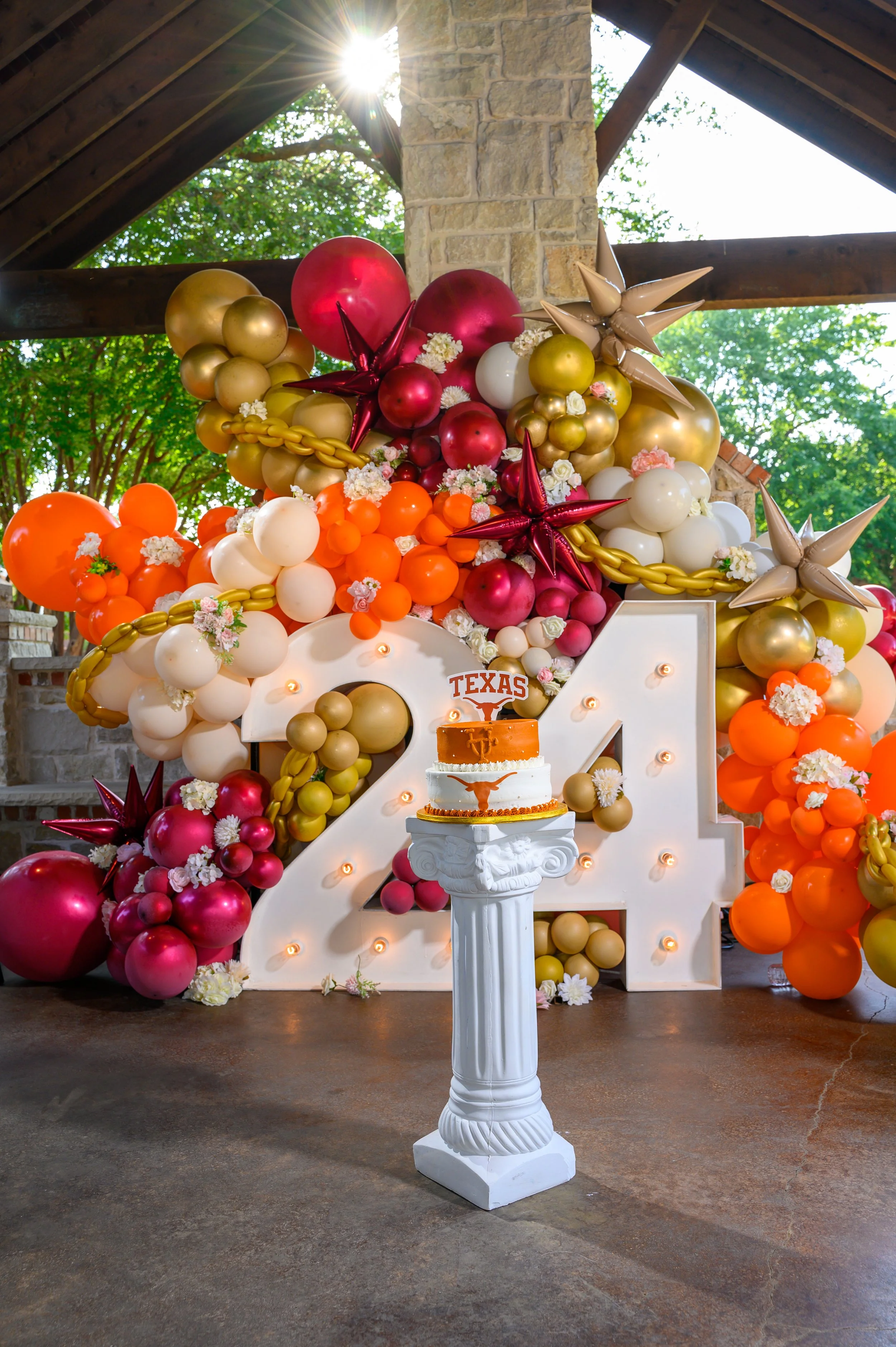 Decorative balloon arrangement in shades of orange, white, gold, and red surrounds a white illuminated