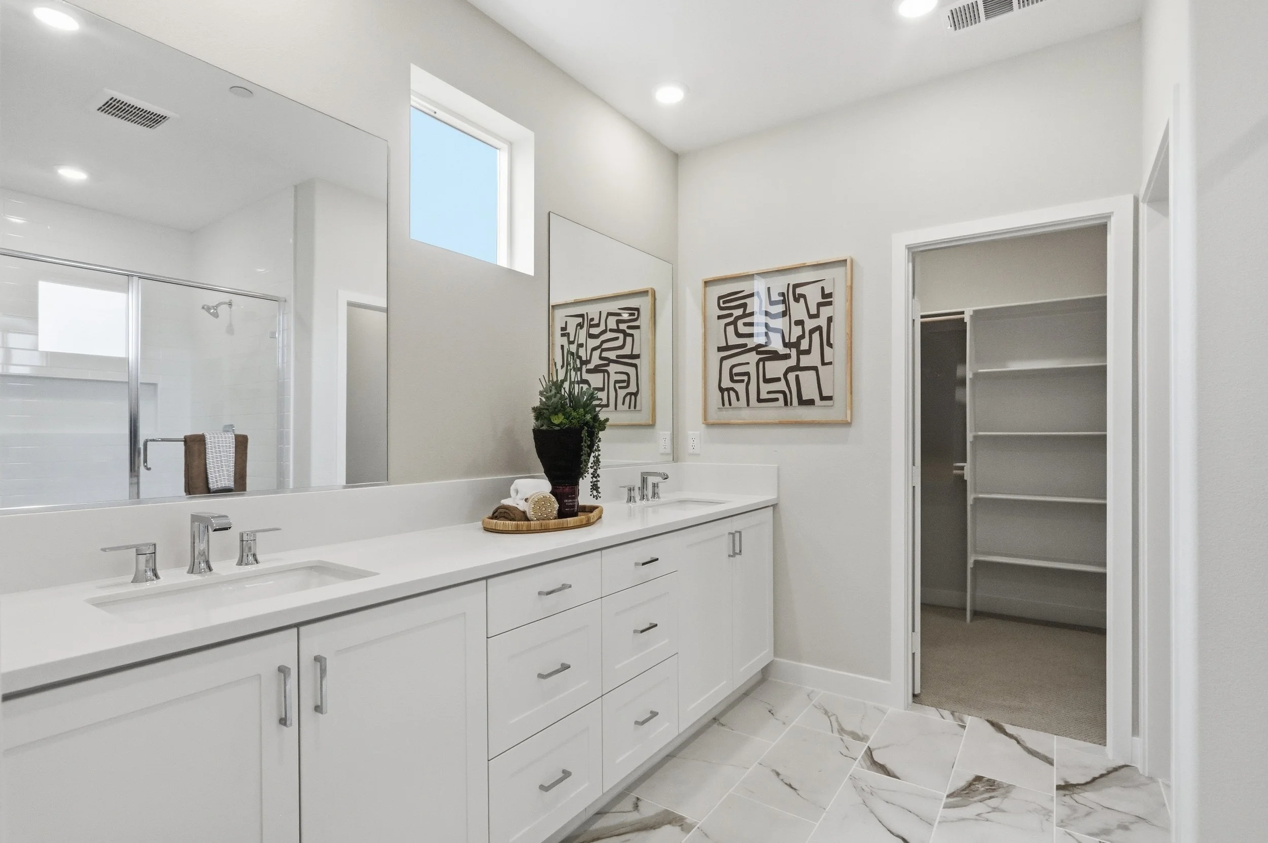 Modern bathroom with white double vanity, large mirror, decorative artwork, and marble floor tiles.