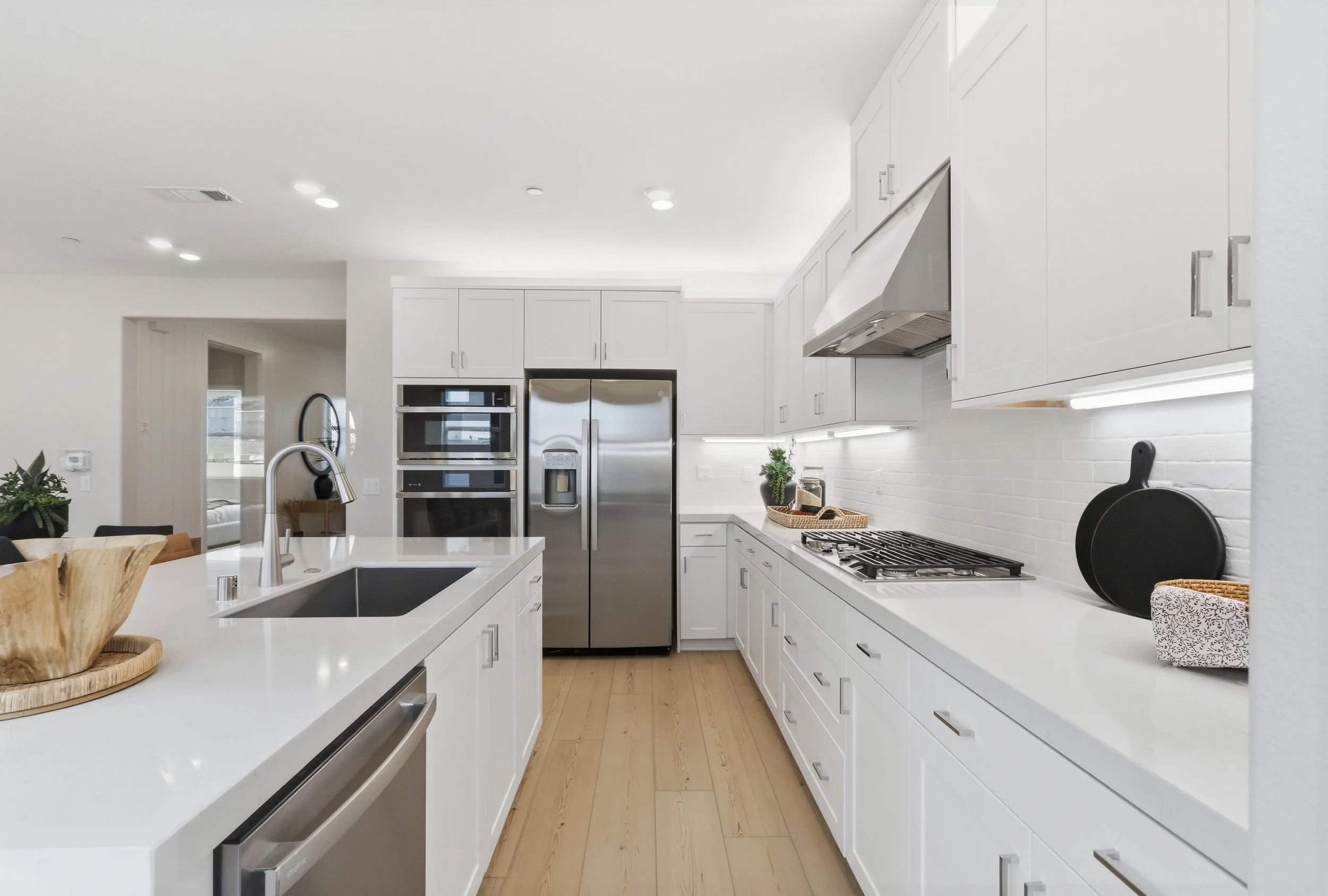 Clean modern kitchen with white cabinets, stainless steel appliances, a white countertop island, wooden flooring, and minimalist decor.