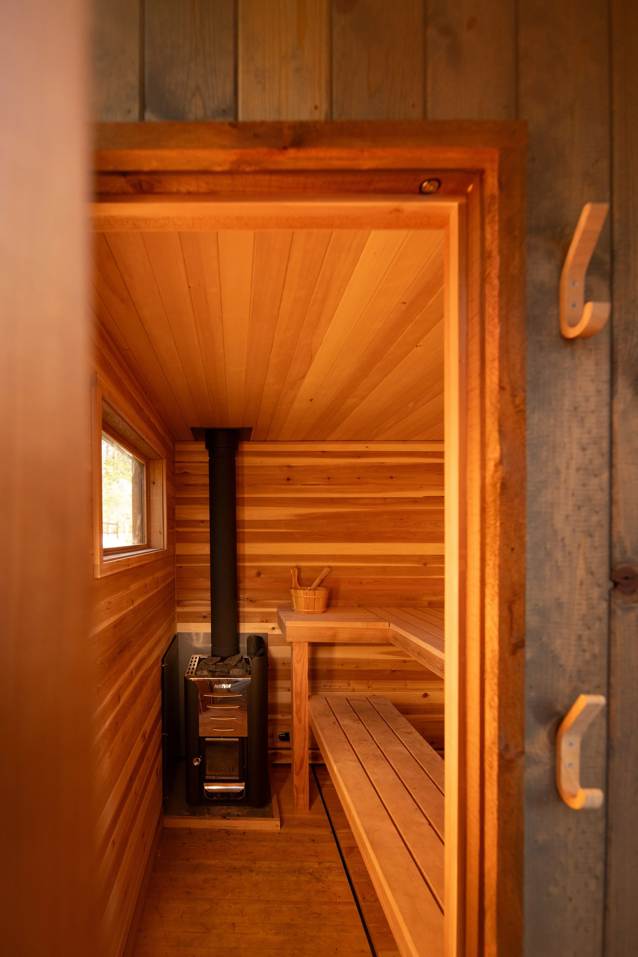 A custom wood-paneled sauna with a custom sauna bench, a small window, and a wood-burning stove in the corner.