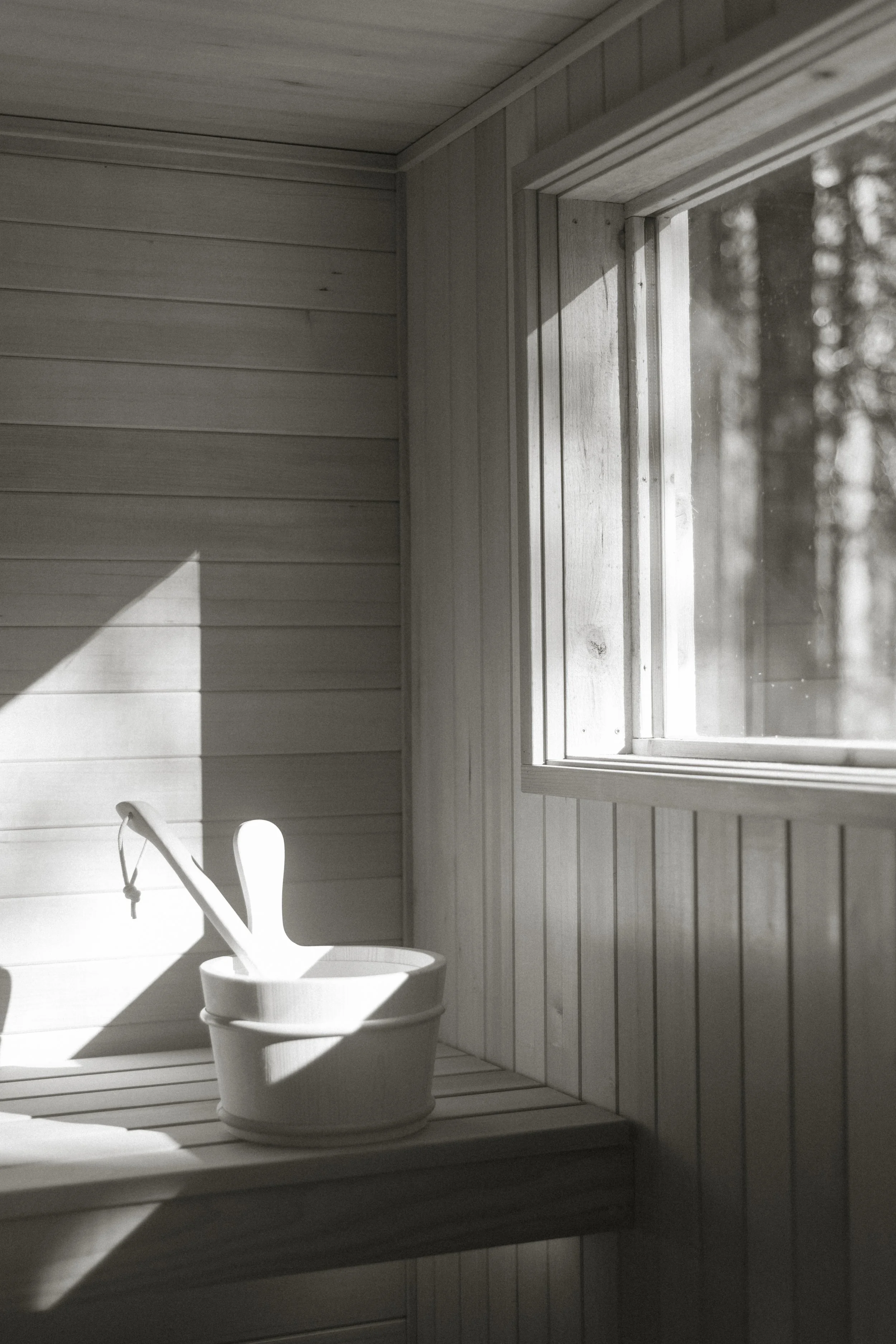 A black and white image of a custom build cedar sauna interior with sunlight streaming through the window.