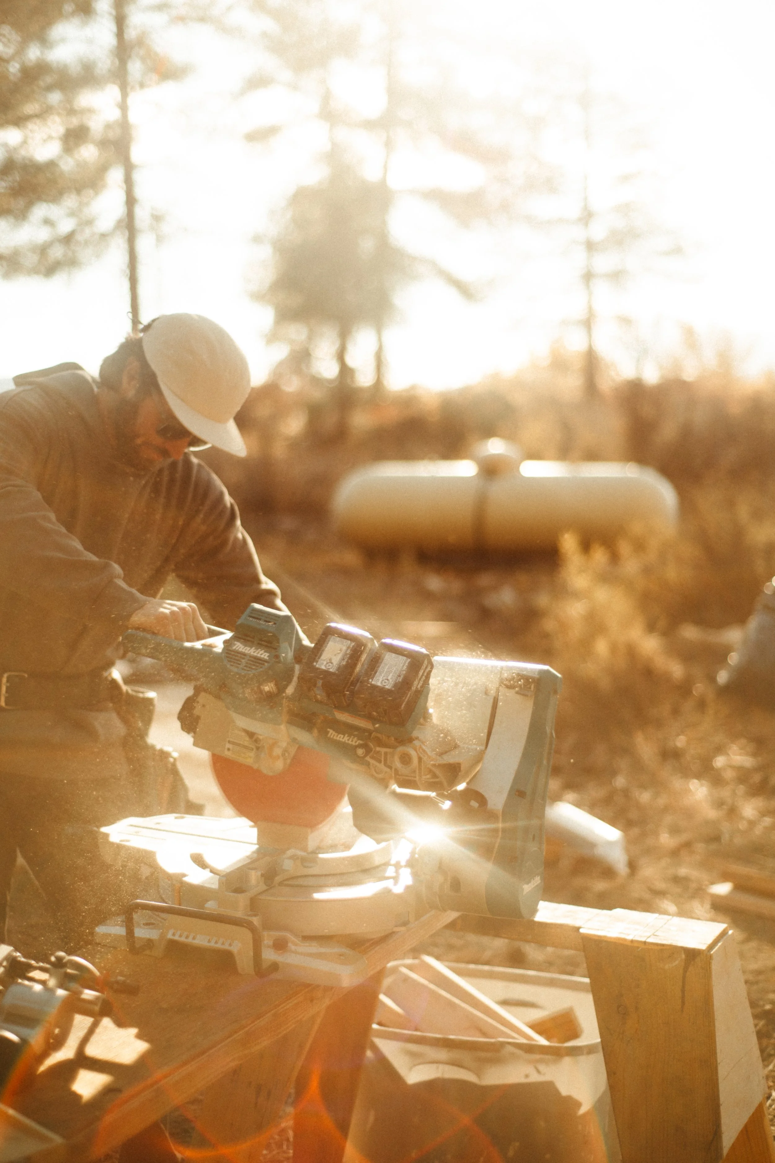 Person working outdoors with power tools on a sunny, forested day.