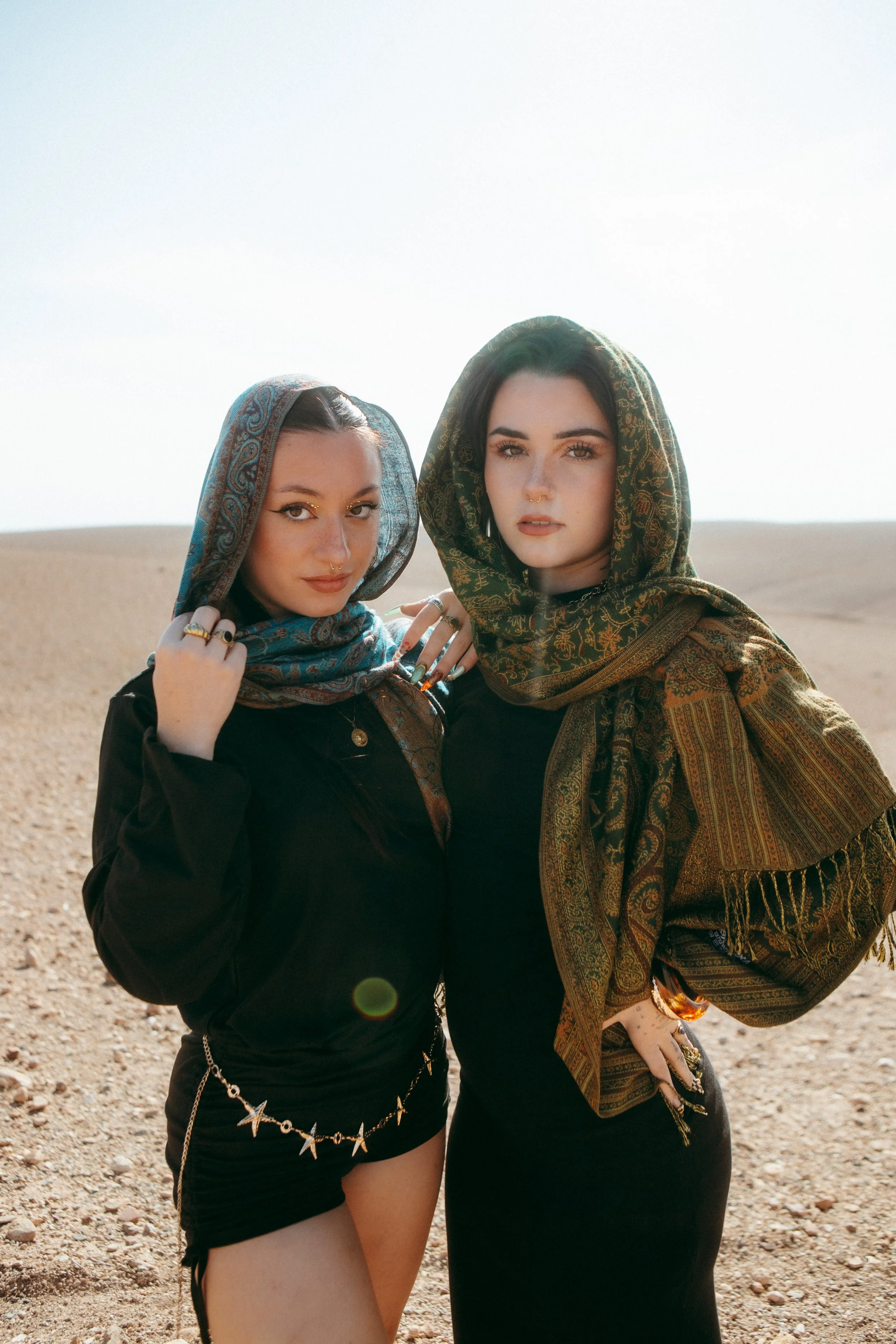 Two women with headscarves standing outdoors on a desert landscape with a clear sky.