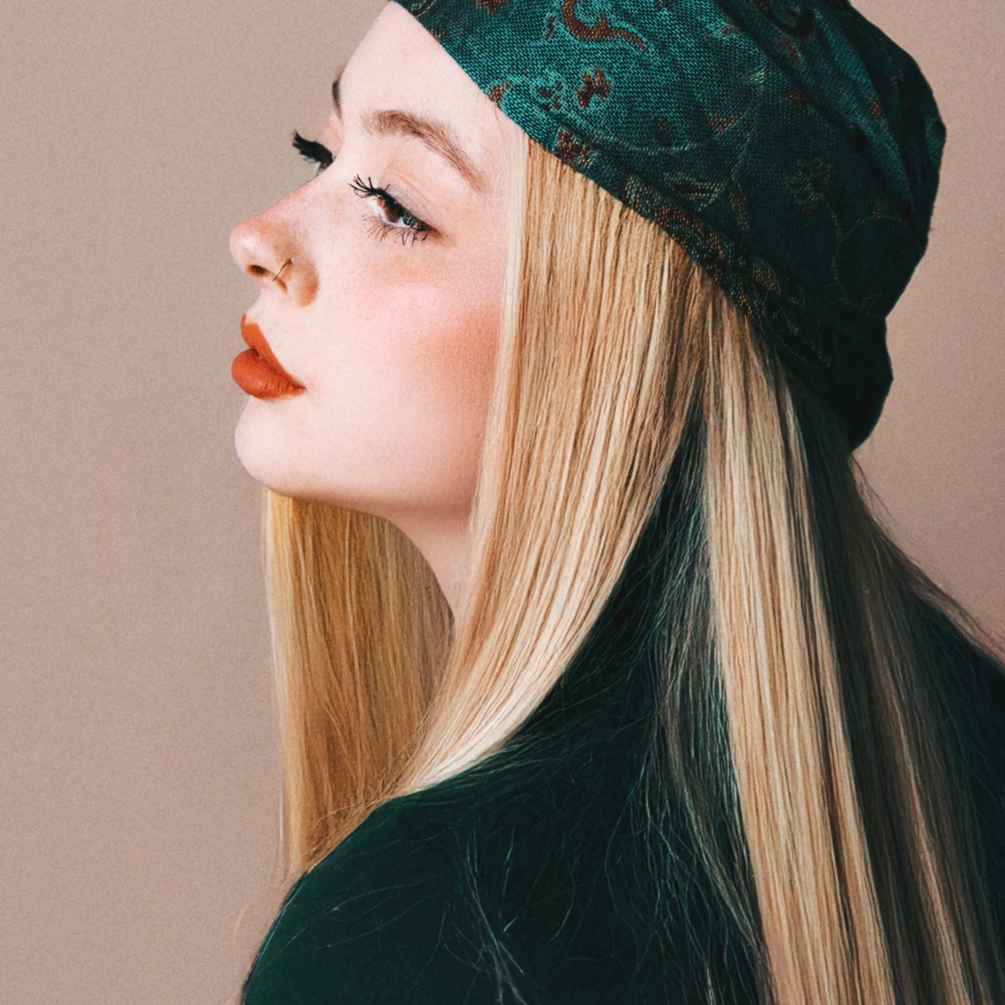 Close-up of a woman's profile with long blonde hair, wearing a green patterned headscarf.