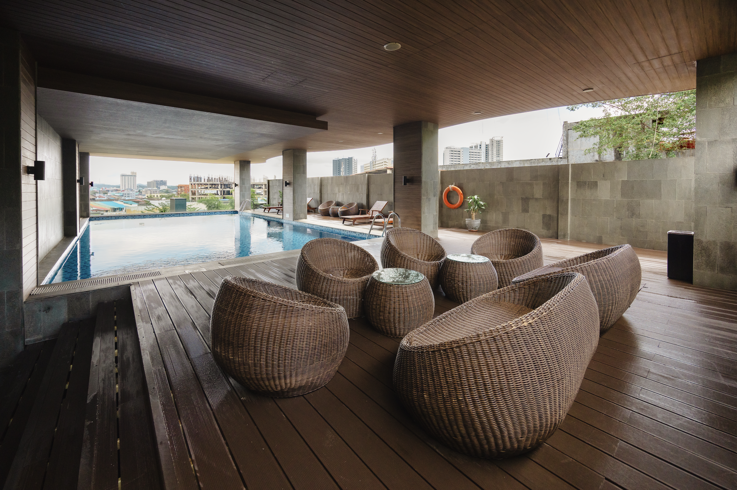 Indoor rooftop pool area with wicker chairs and a view of city buildings in the background.