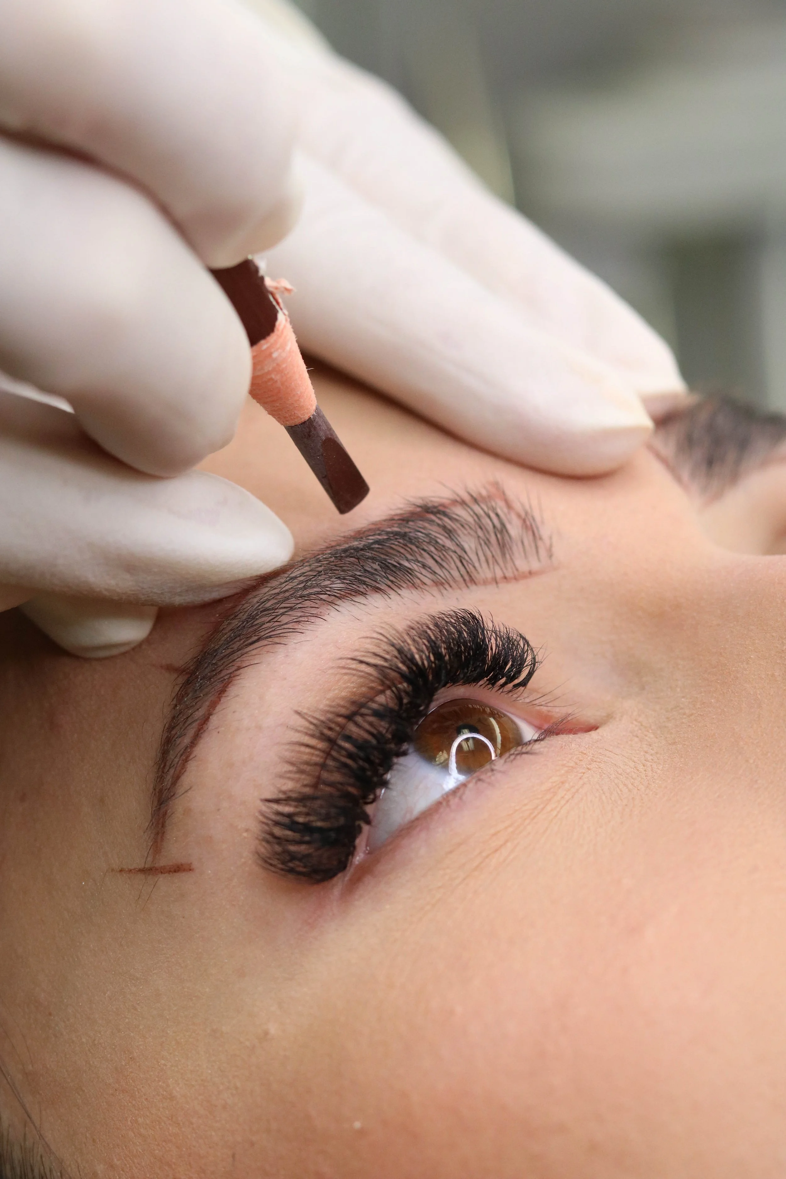 A person receiving an eyebrow threading procedure, with a focus on the person's eye, eyebrow, and the technician's gloved hand holding a threading tool close to the brow.