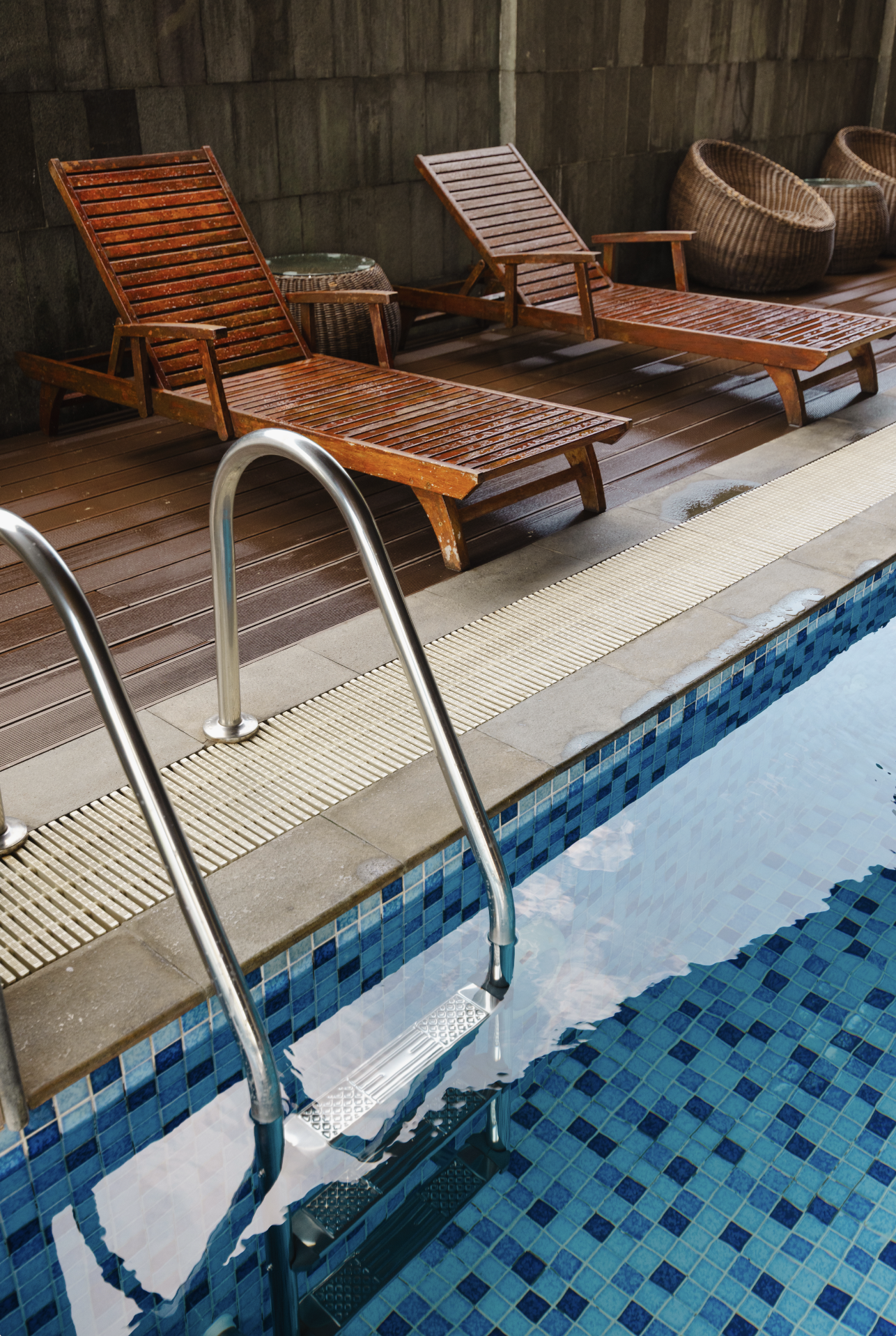 Wooden lounge chairs beside a swimming pool with steps leading into the water.