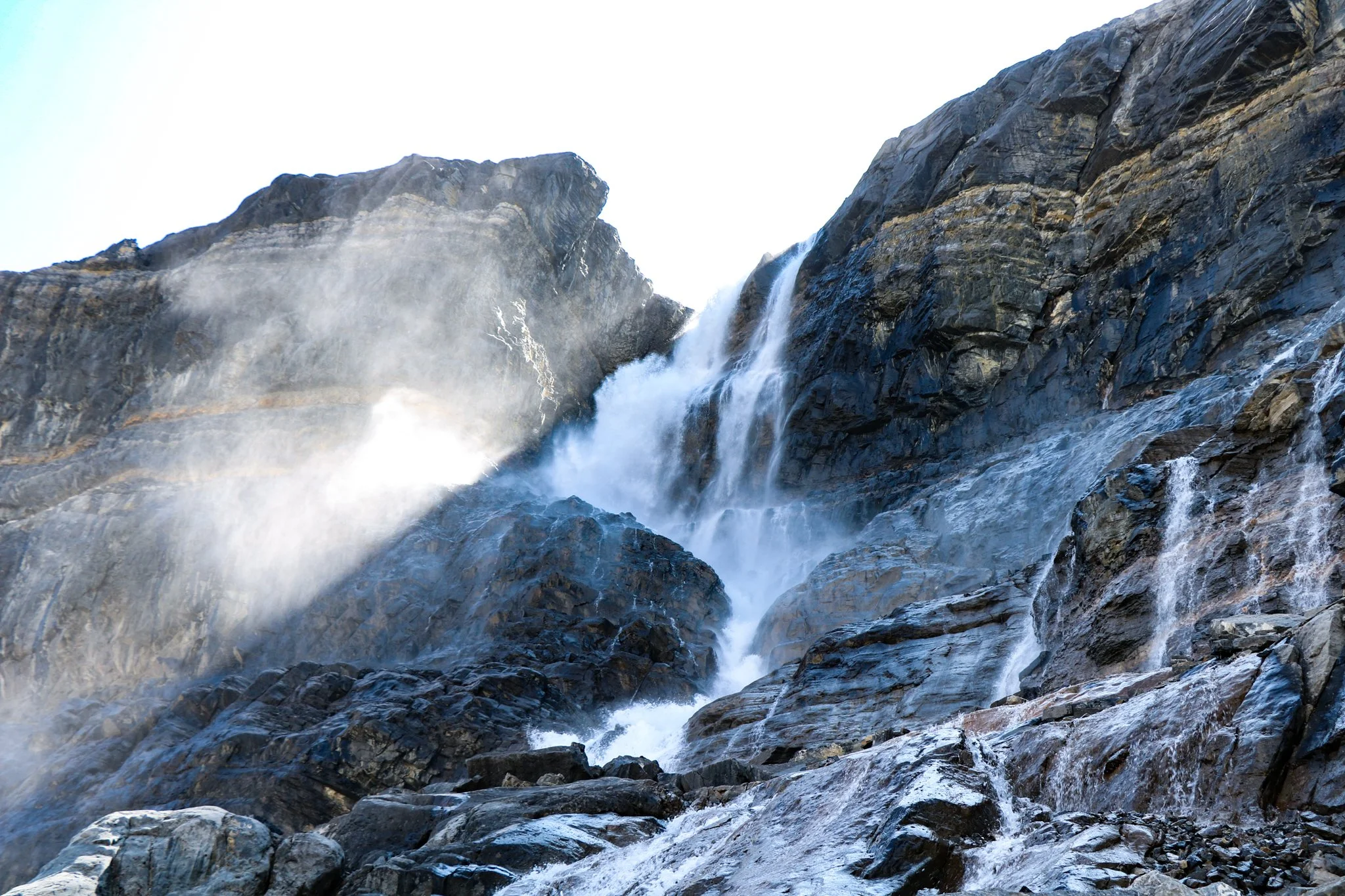 A powerful waterfall cascading down dark rocky cliffs with mist rising at the top and water flowing over rocks at the bottom