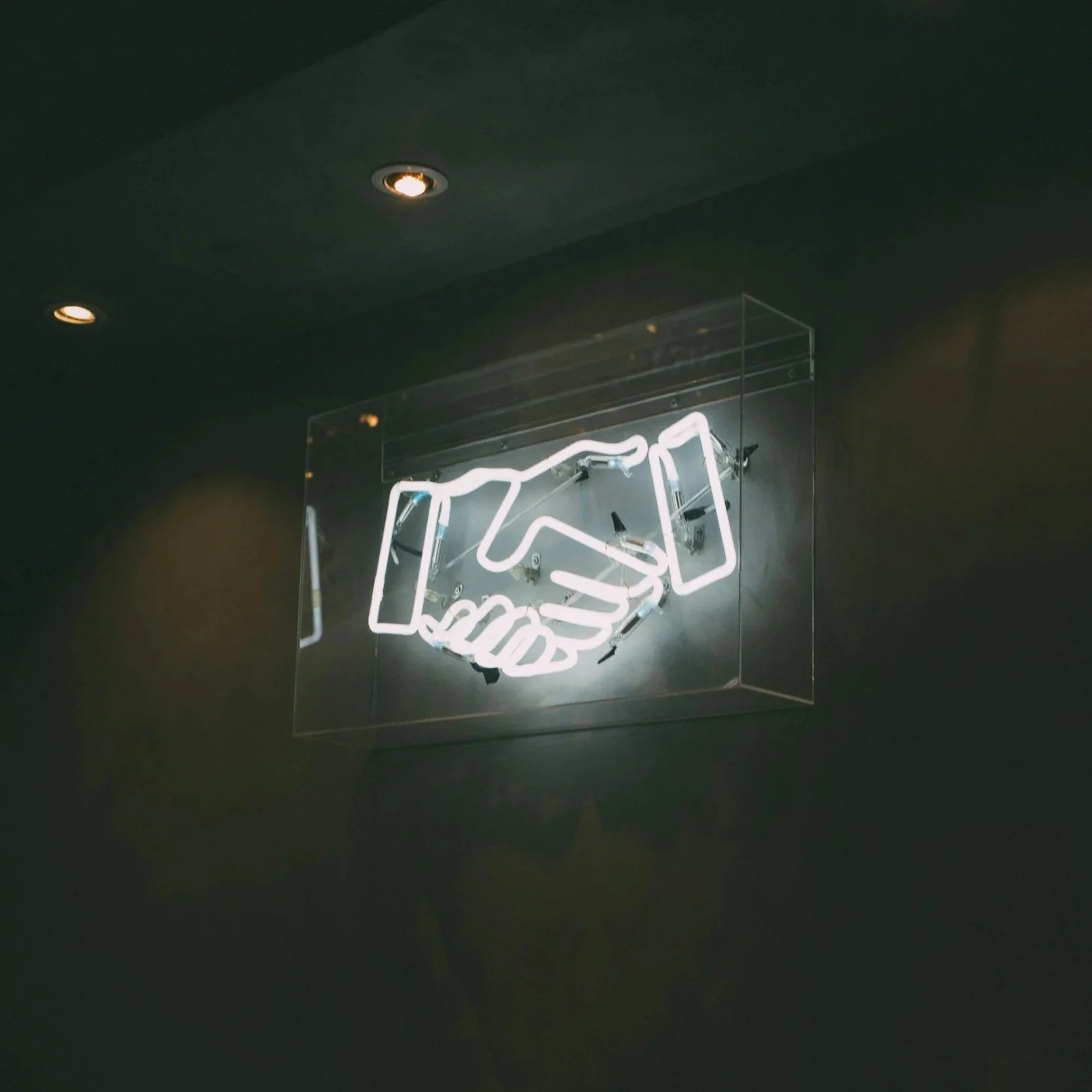 A neon light forms the shape of two hands shaking.