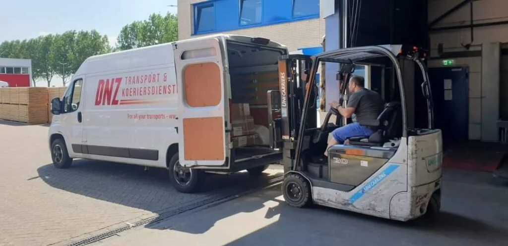 Man rijdt een elektrische vorkheftruck uit een wit vervoersbus met de tekst 'DNZ Transport & Koeriersdienst'.