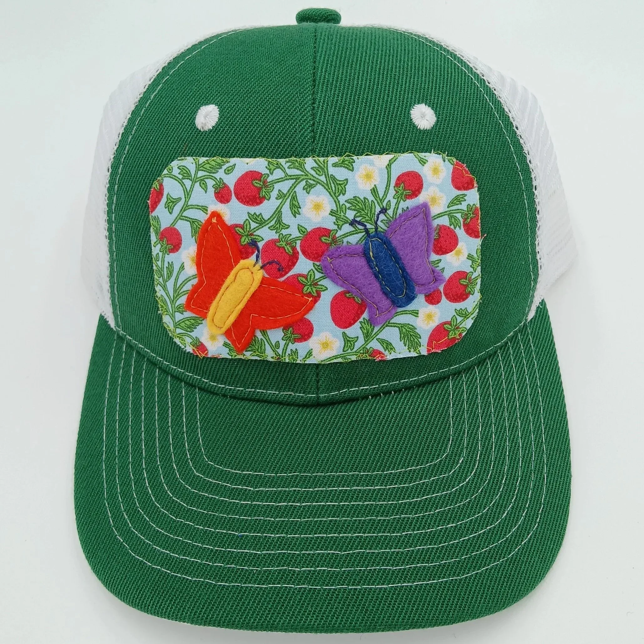 A green baseball cap with a white mesh back and a fabric front featuring embroidered colorful butterflies and red berries on a light background.