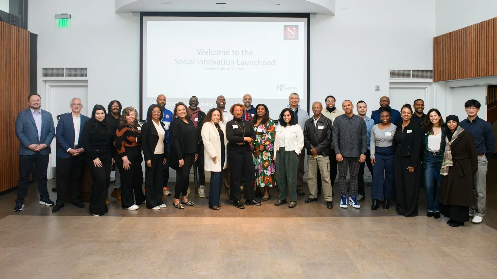 Group of diverse people attending the Social Innovation Launchpad event in a conference room, standing in front of a large screen displaying the event title and date.