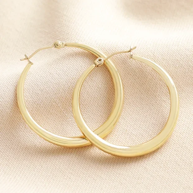 Gold hoop earrings on a light-colored fabric surface.